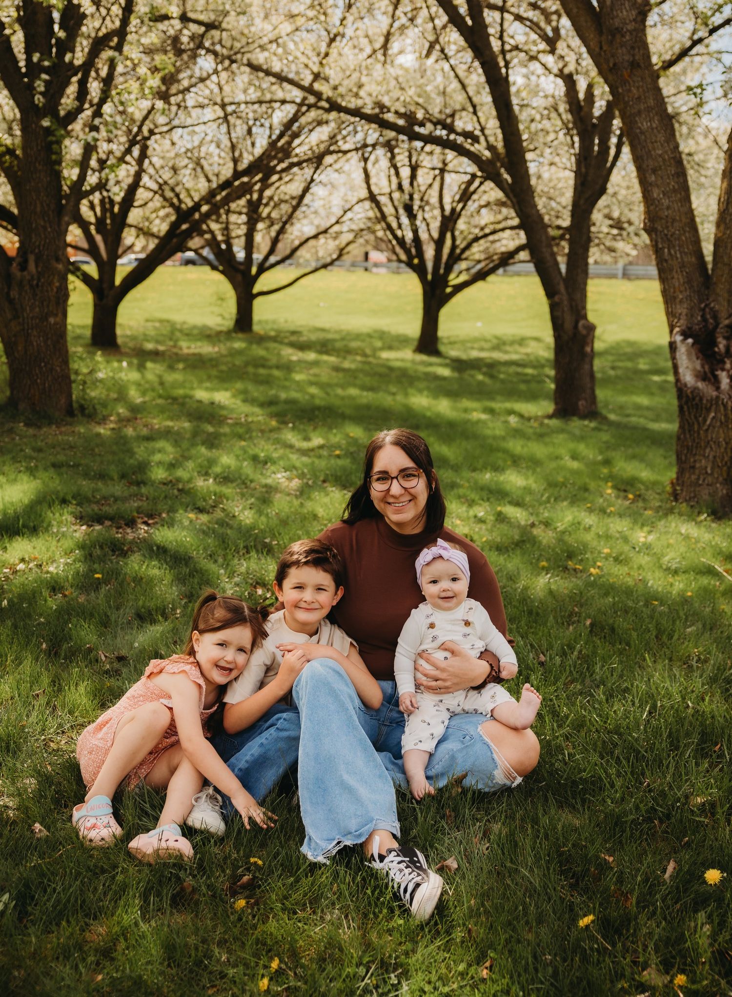 A family relaxes together under blossoming spring trees on a grassy hillside during an outdoor photo session.