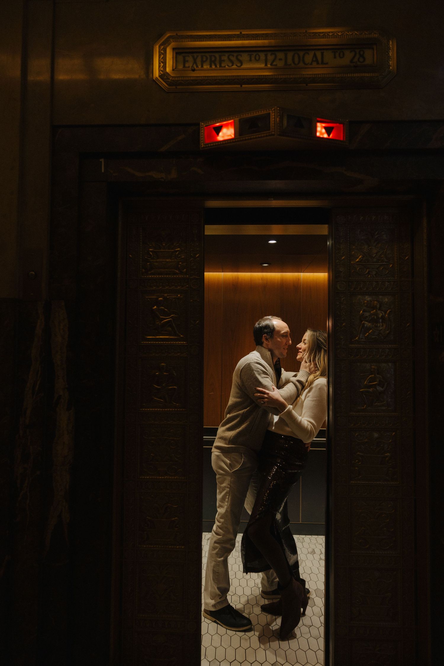 Couple sharing a romantic moment in an ornate vintage elevator with warm glowing lights.
