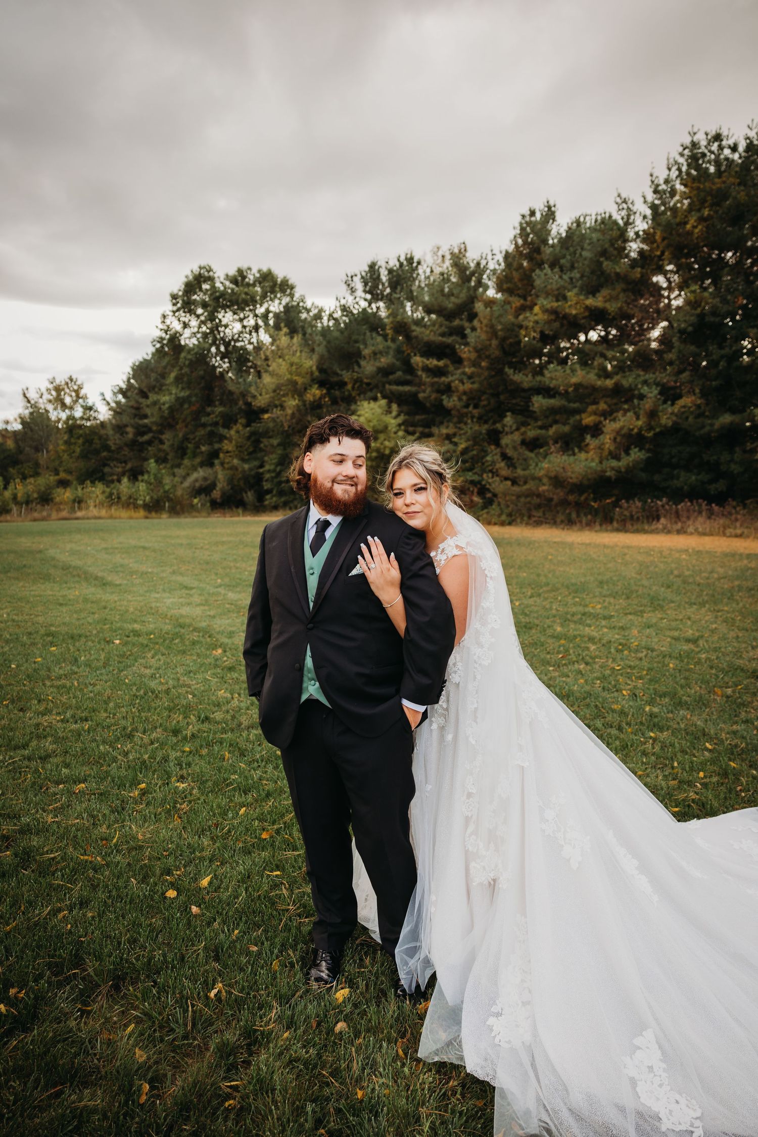 Outdoor wedding portrait with pine trees and cloudy sky backdrop.