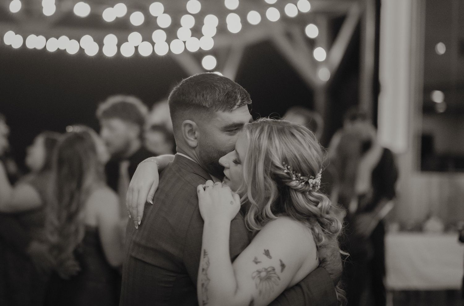 A couple shares an intimate slow dance under twinkling lights at their wedding reception.
