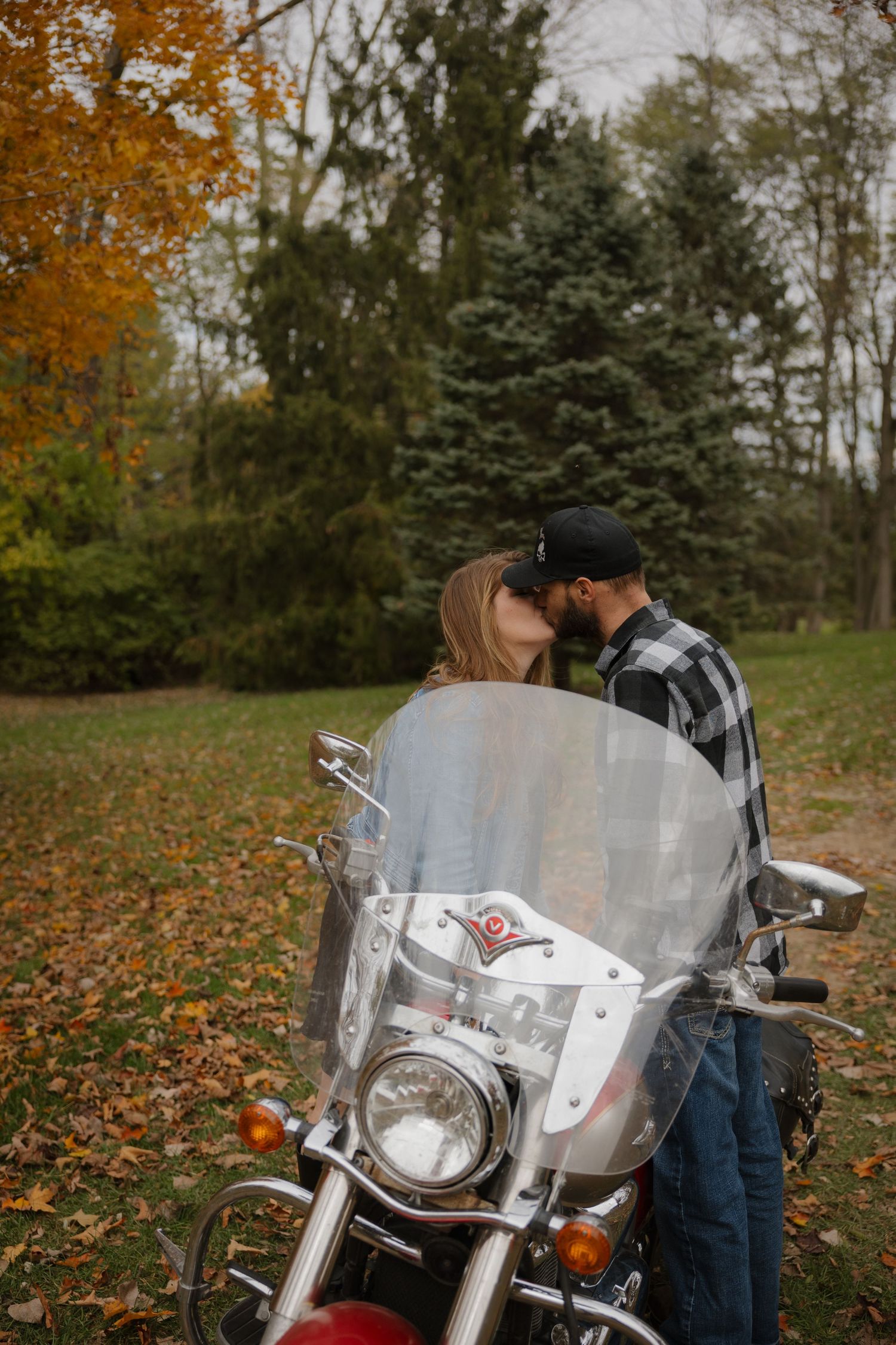 A silver motorcycle with a windshield parked on autumn leaves with trees in the background.