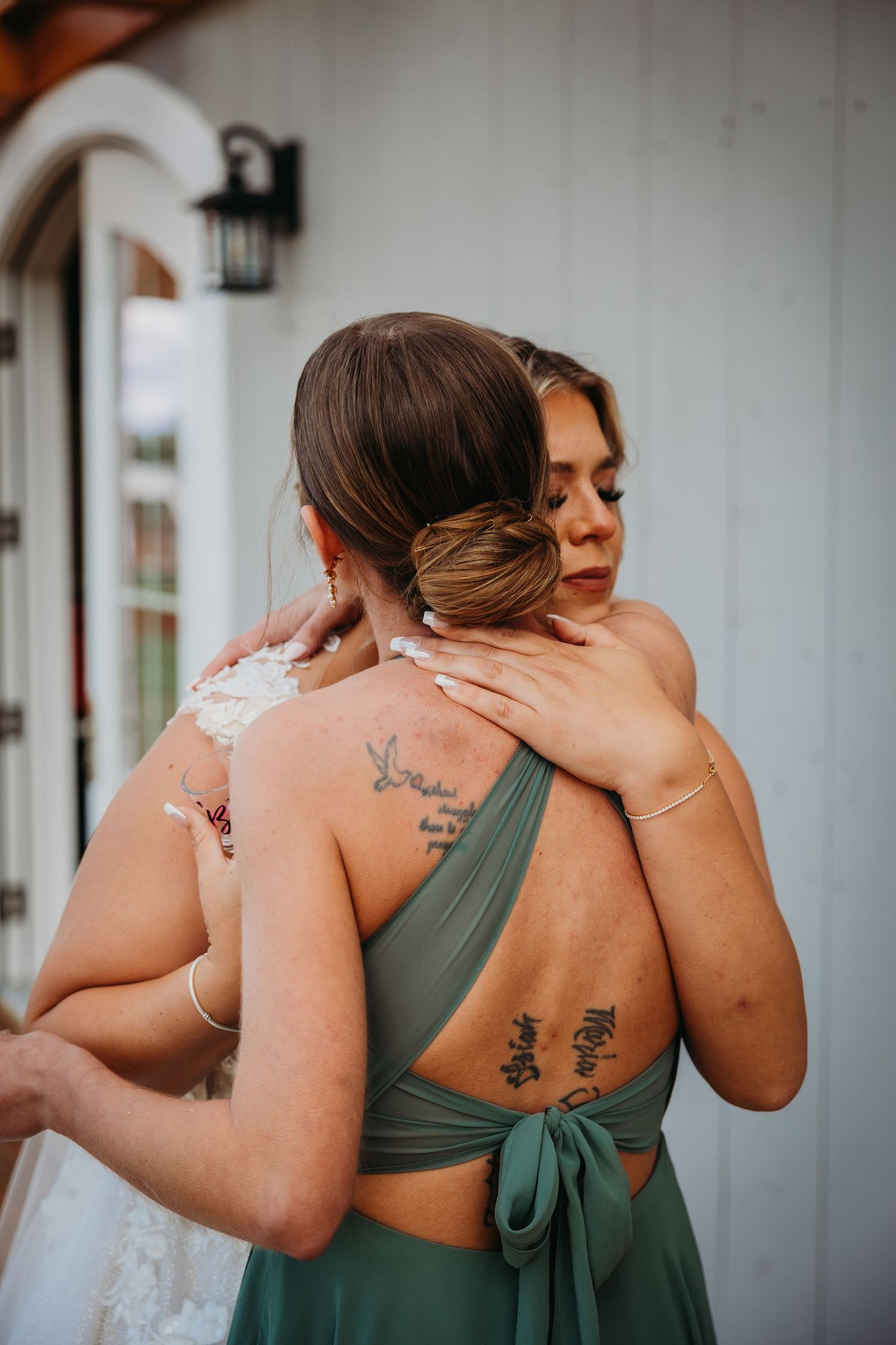 Emotional embrace between bride and bridesmaid showing visible tattoos.