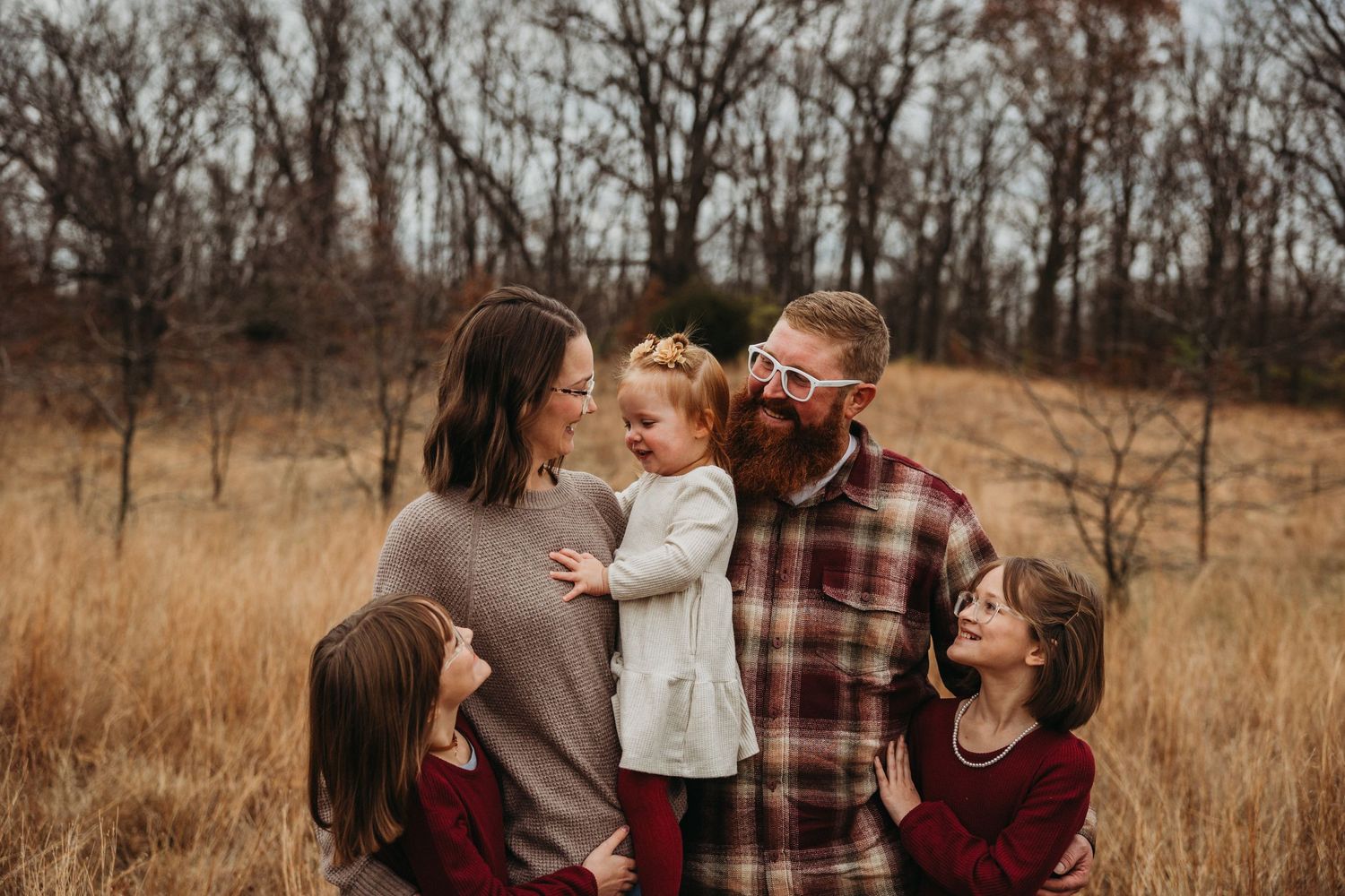 Family portrait session in autumn field with coordinated burgundy outfits.