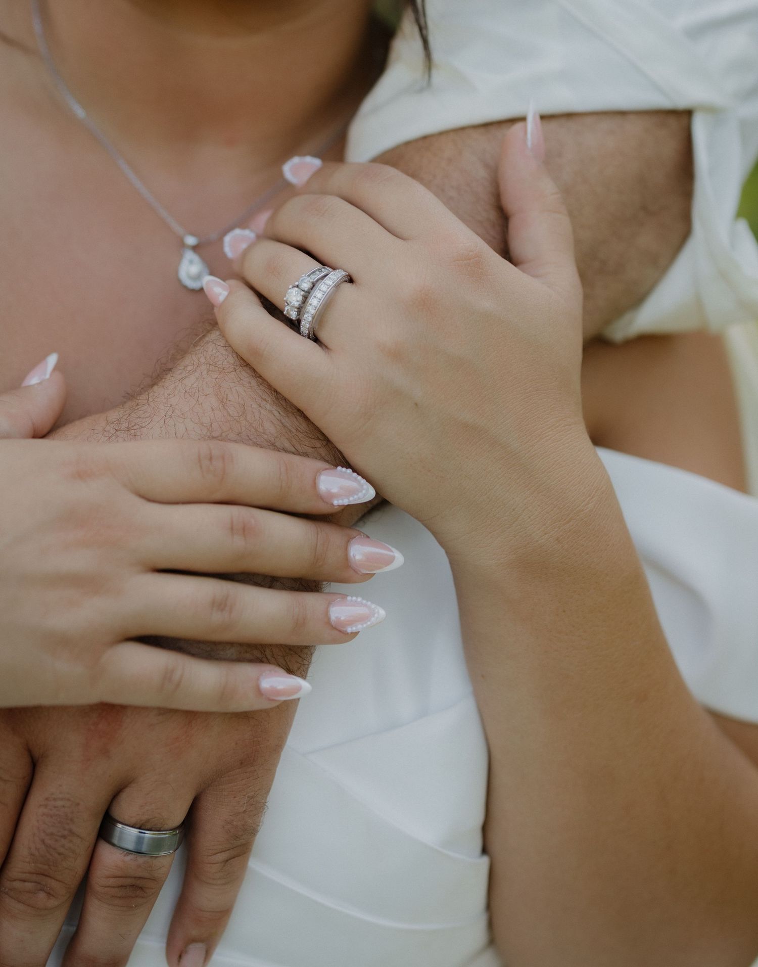 Close-up of bride and groom hands showing wedding rings, with bride wearing diamond engagement ring and French manicure.