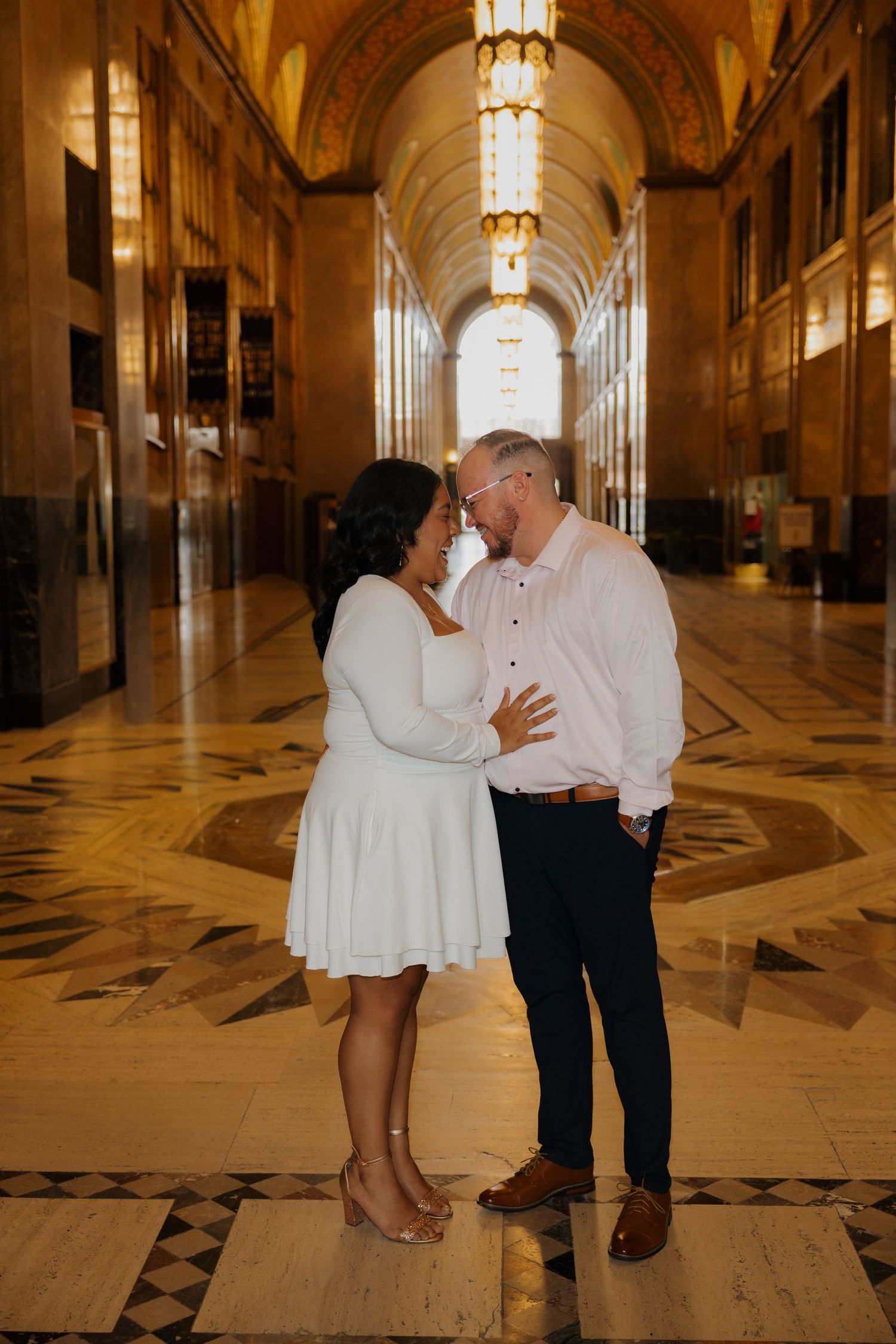 Couple sharing a romantic moment in an elegant marble hallway with ornate ceiling and warm golden lighting.
