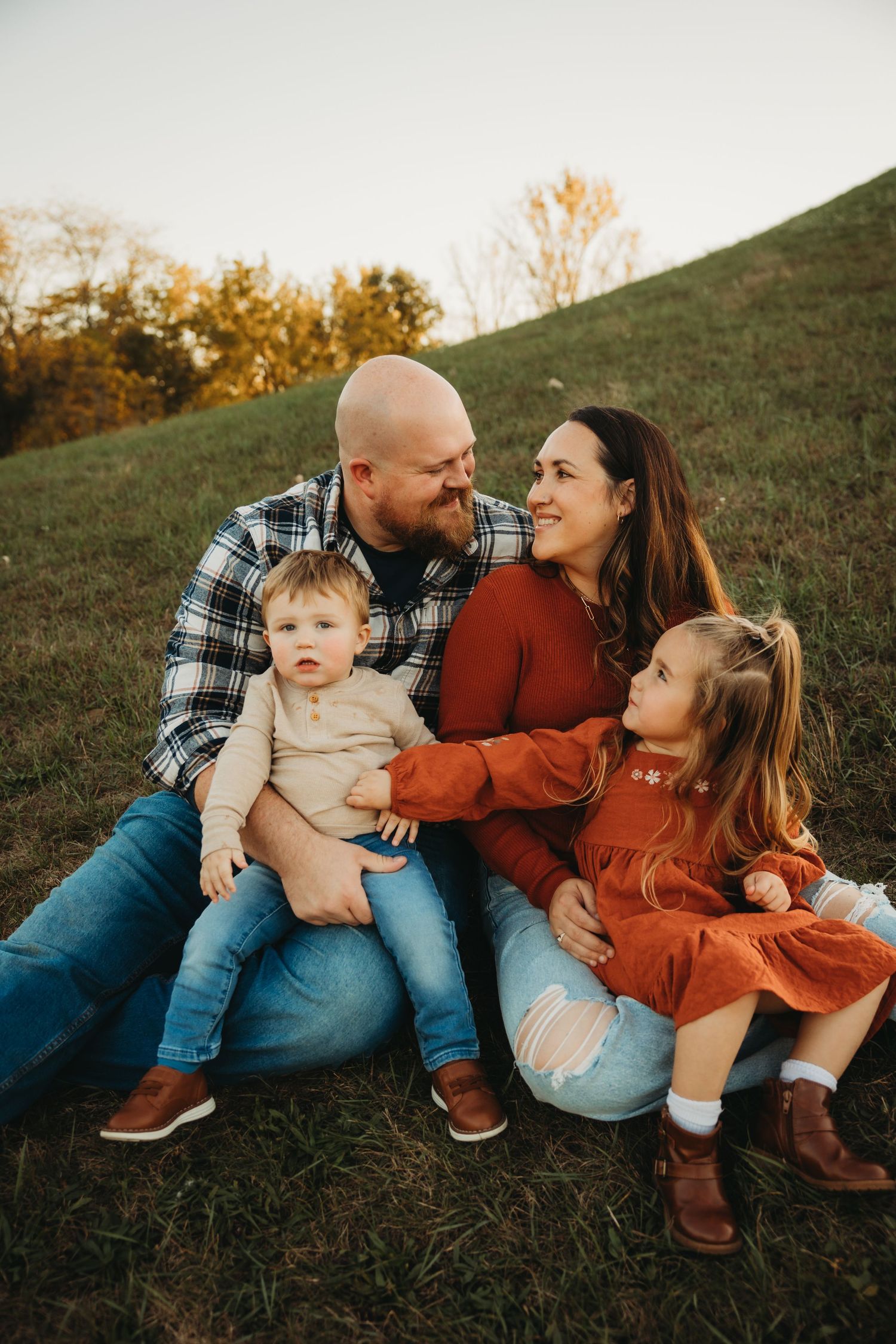 Family of four sharing loving candid moment while sitting together on grassy slope.