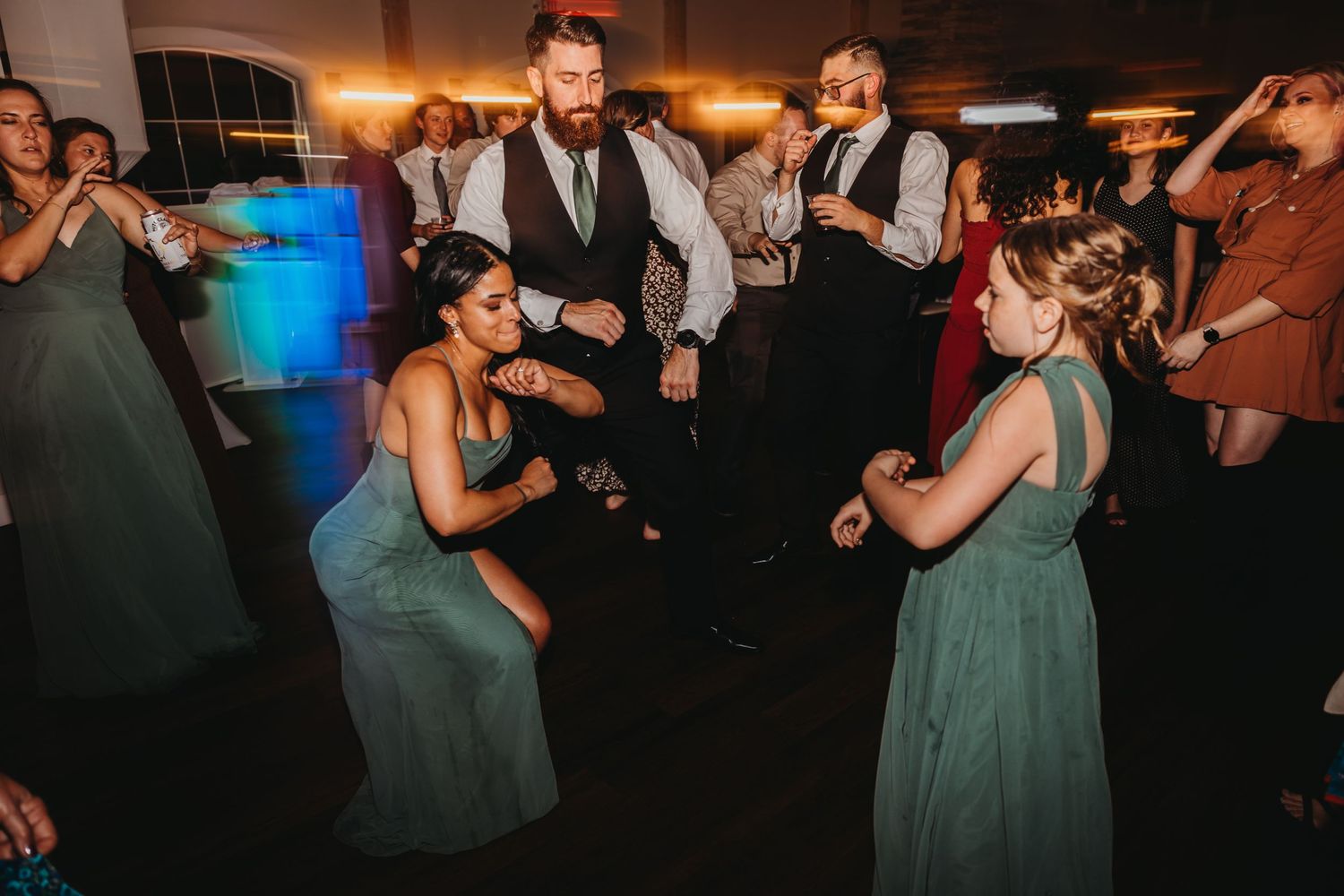 Wedding guests dancing energetically at a reception with bright blue lighting and formal attire.