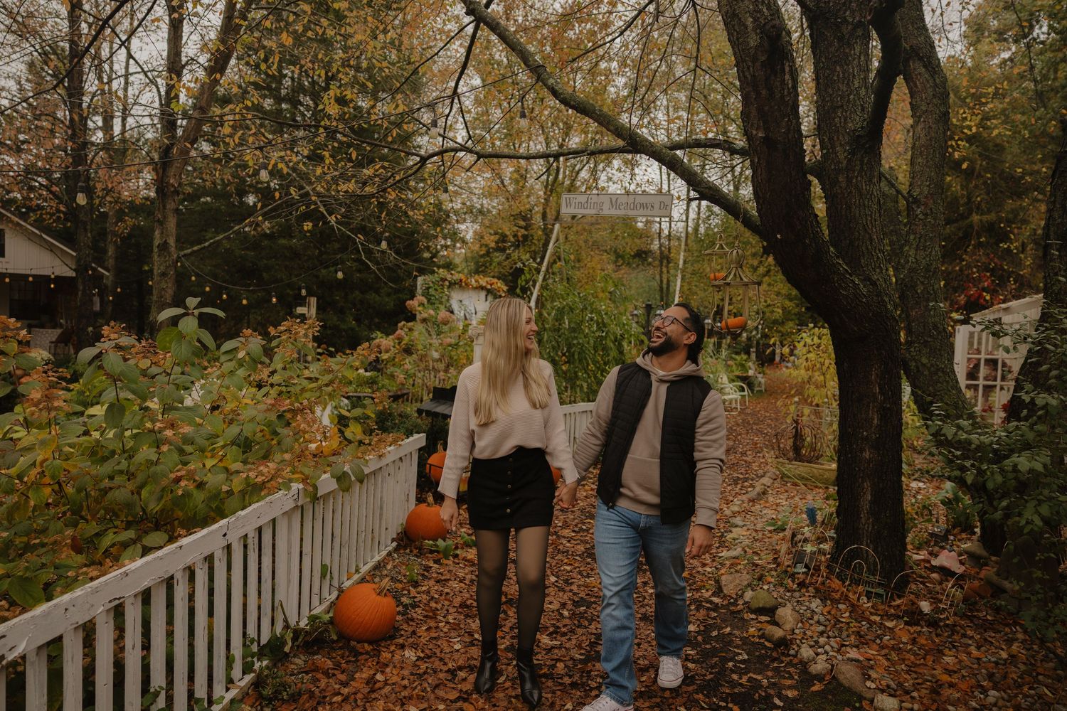 People walking along a leaf-covered path surrounded by autumn trees with orange and yellow foliage.