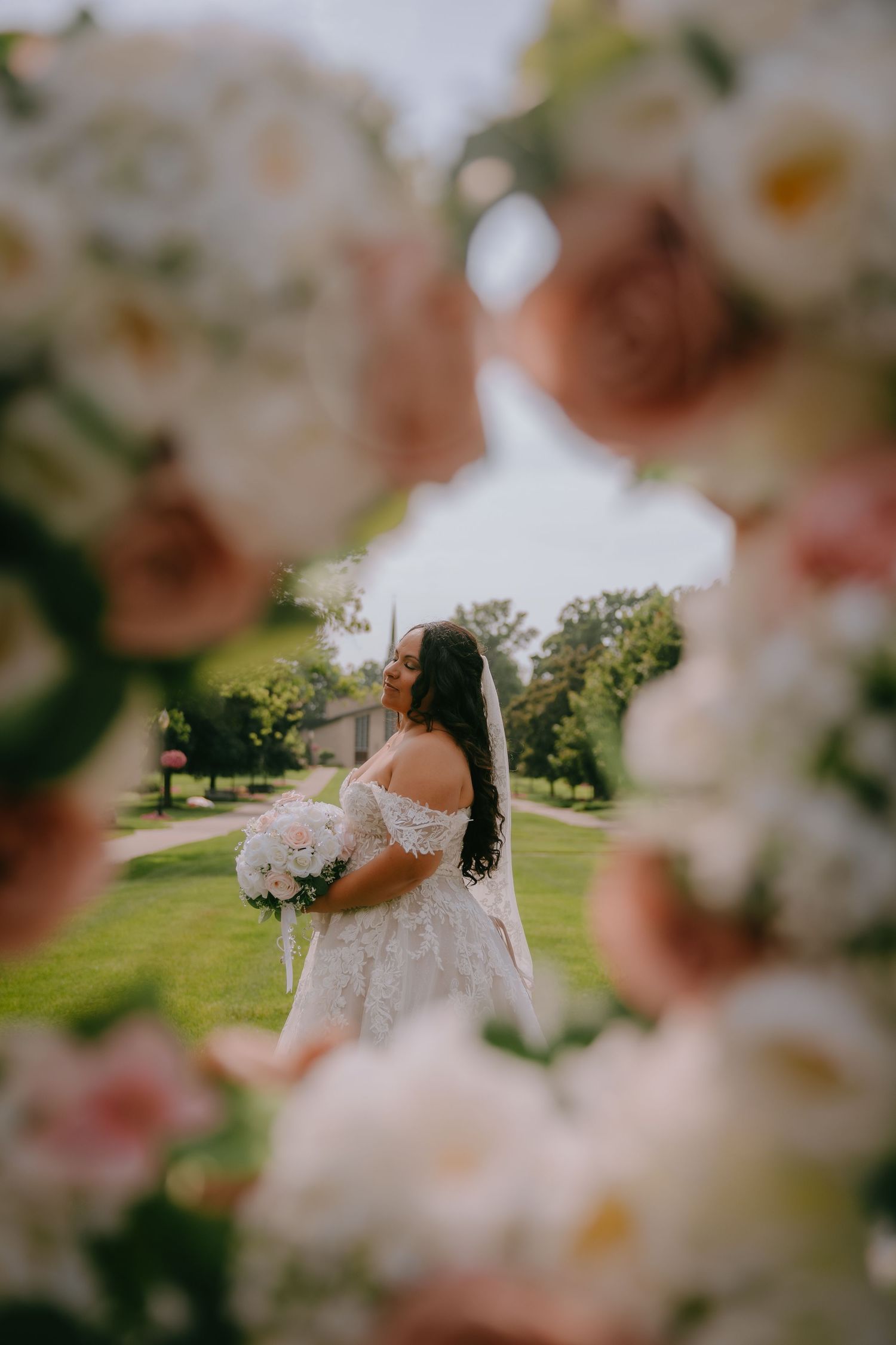 Artistic wedding photography through soft blush pink and white flowers framing a sunny outdoor garden scene.
