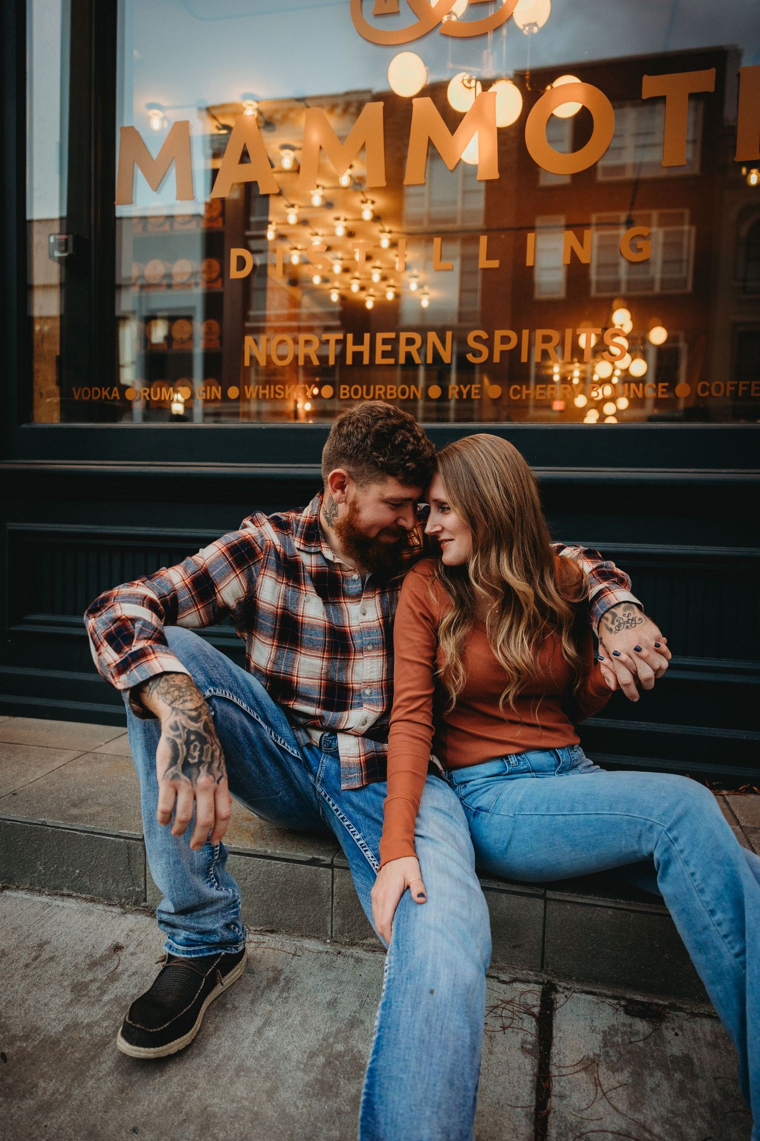 Couple sitting outside illuminated storefront with string lights in evening setting.