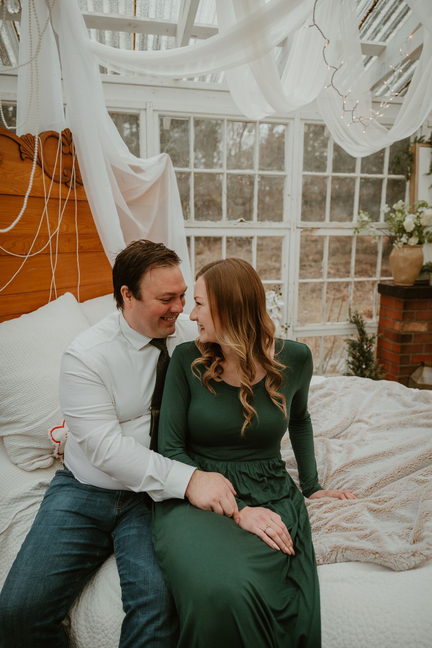 A couple shares an intimate moment together in a sunlit room with white drapes and floral decor.