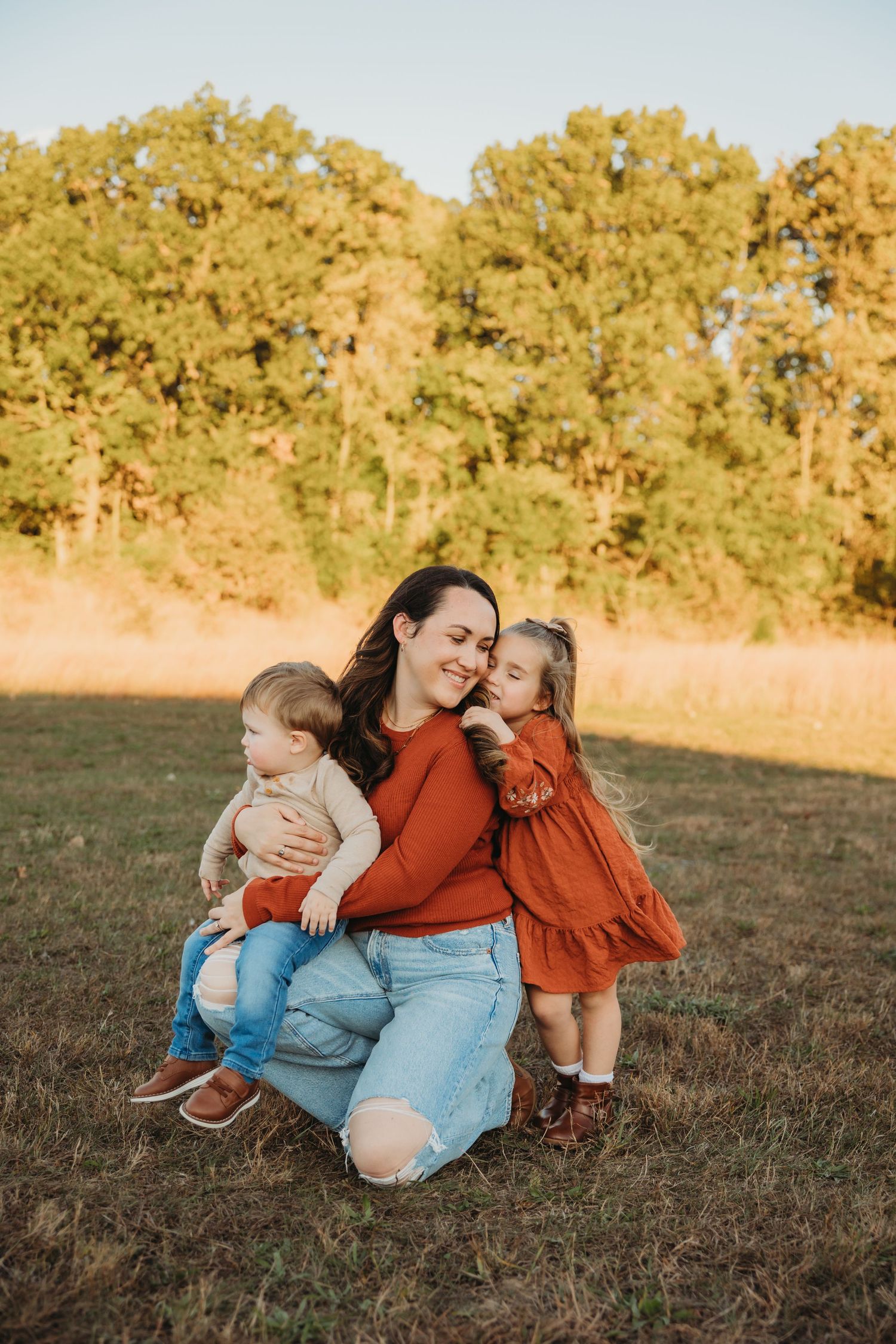 Mother sharing tender moment with two small children during outdoor autumn photoshoot.