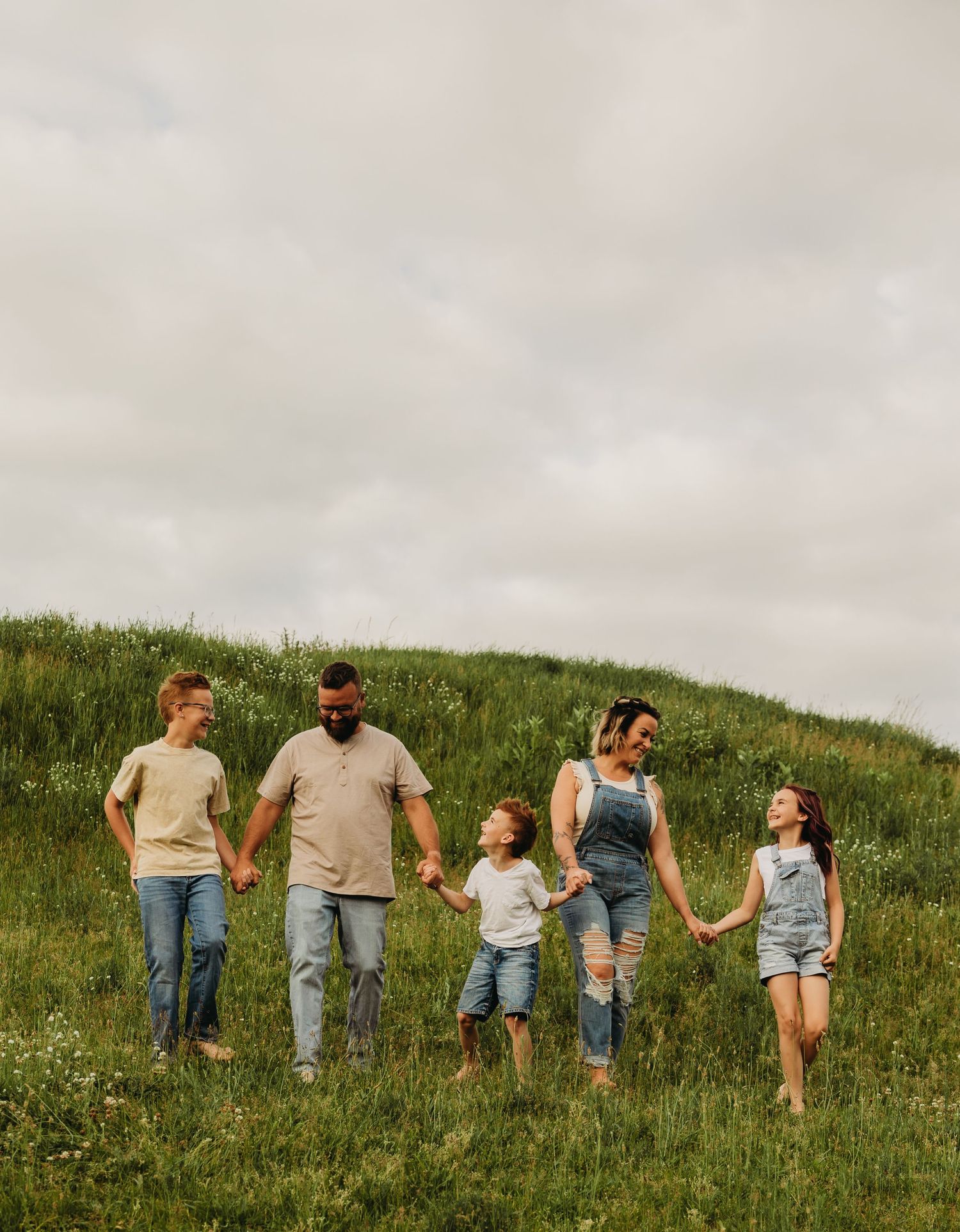 Group walking together up green hillside with wildflowers on overcast day.