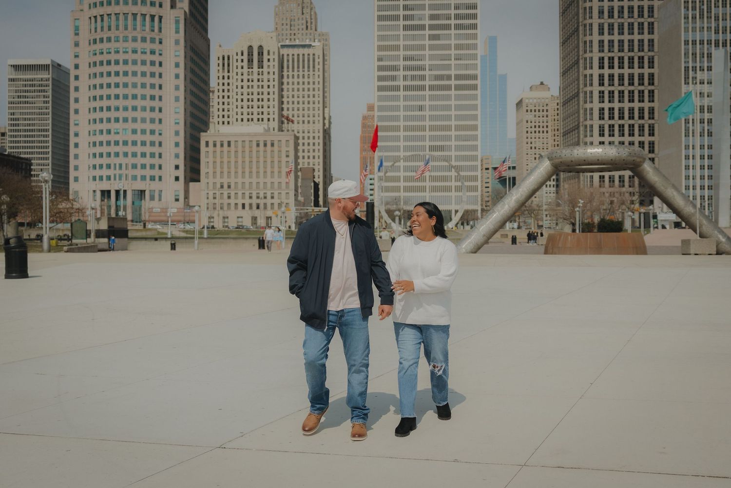 Couple walking hand in hand in front of a city skyline on a sunny day.