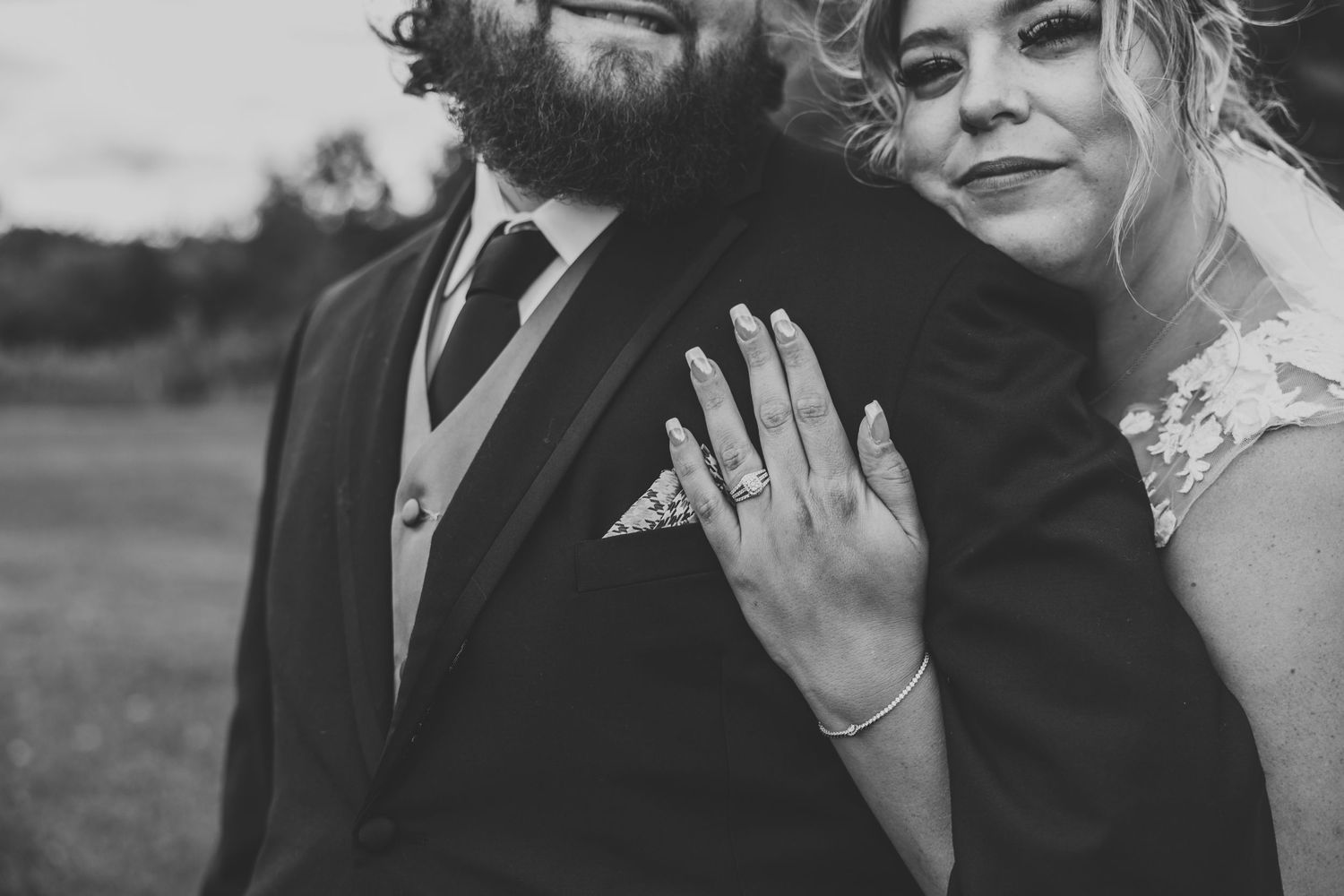 Black and white close-up showing wedding ring and formal attire details.