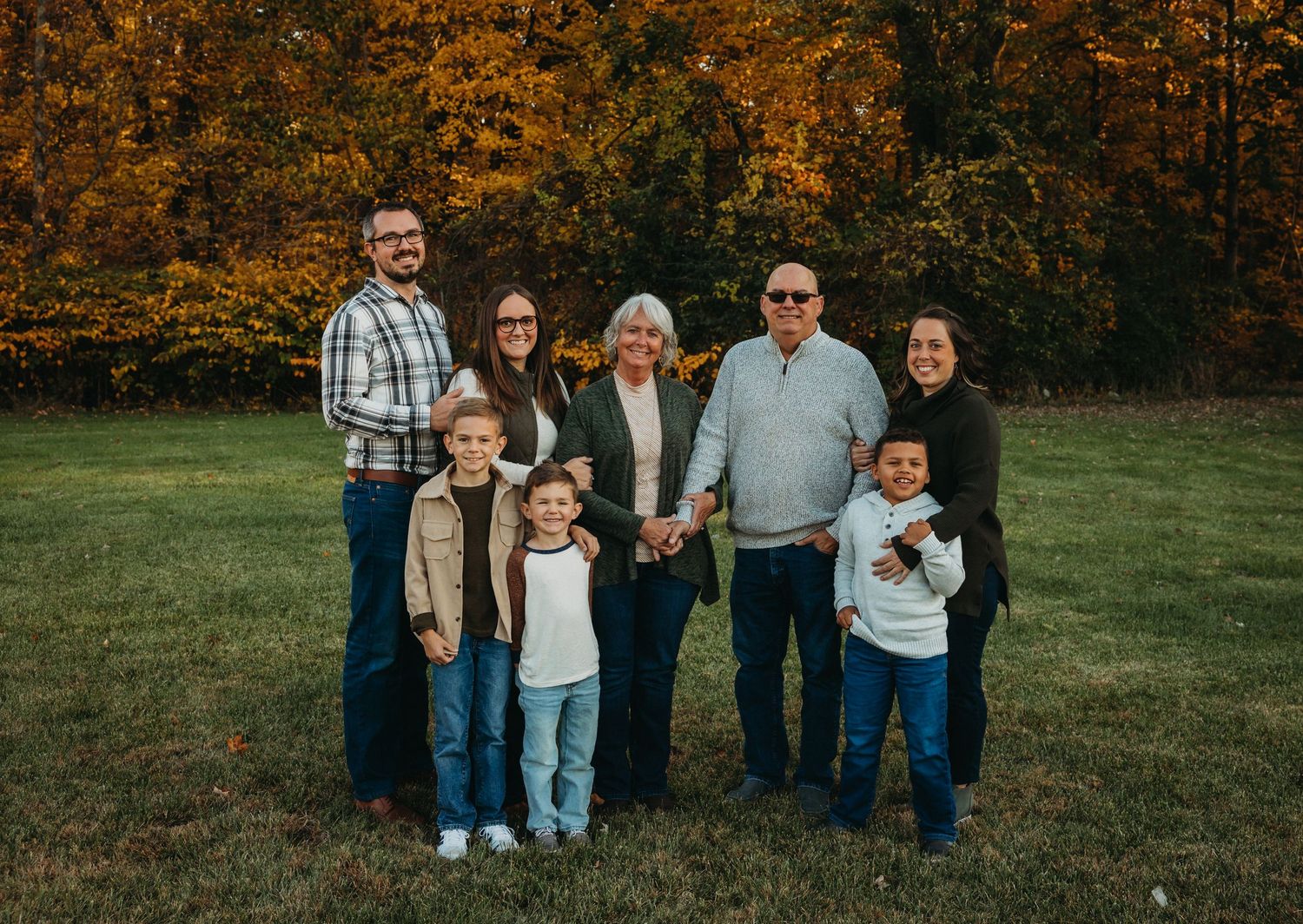 Extended family group portrait with multiple generations against autumn foliage backdrop.