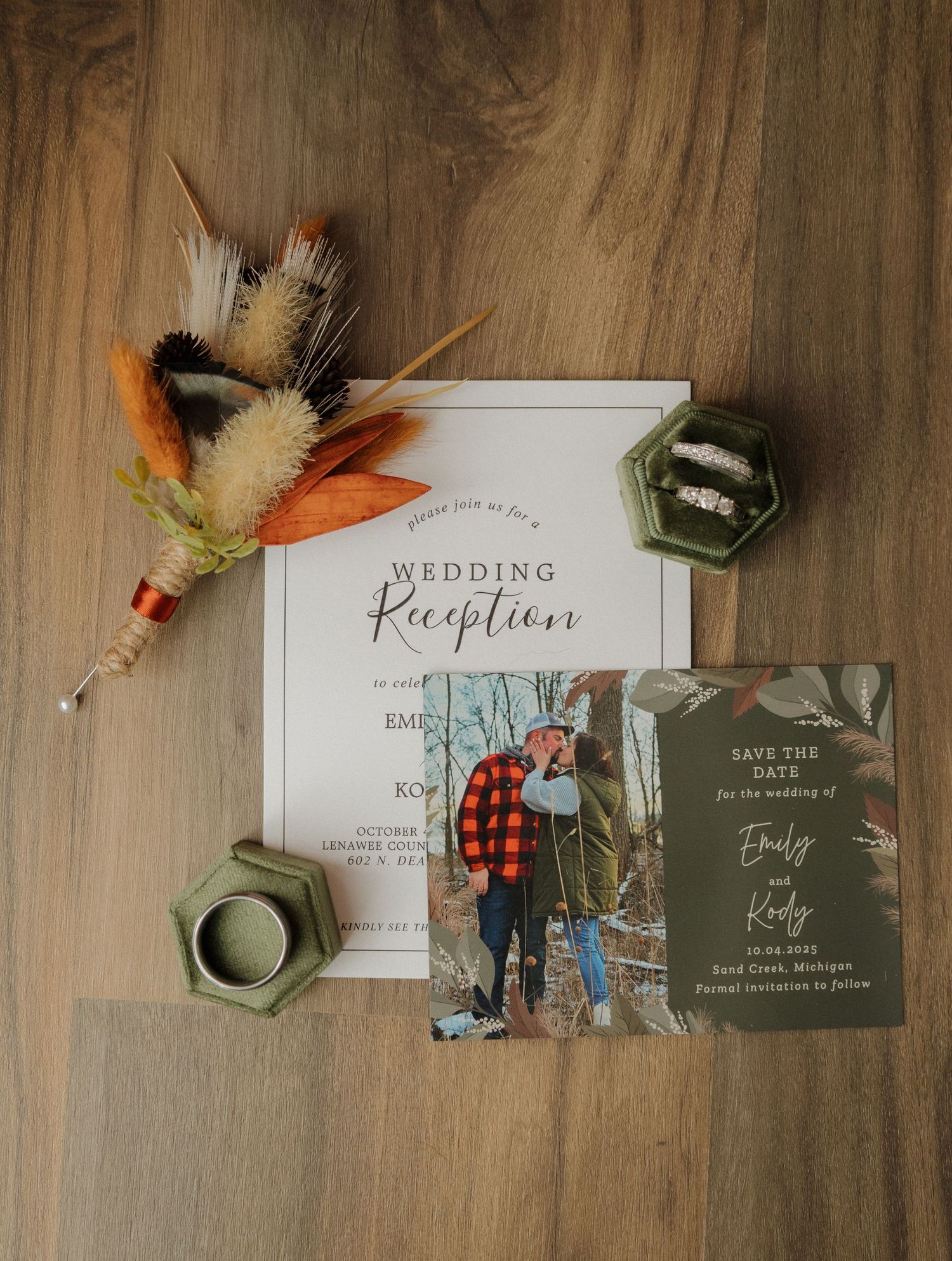 Wedding reception invitation suite with save the date card, ring boxes, and dried floral arrangement on wood surface.