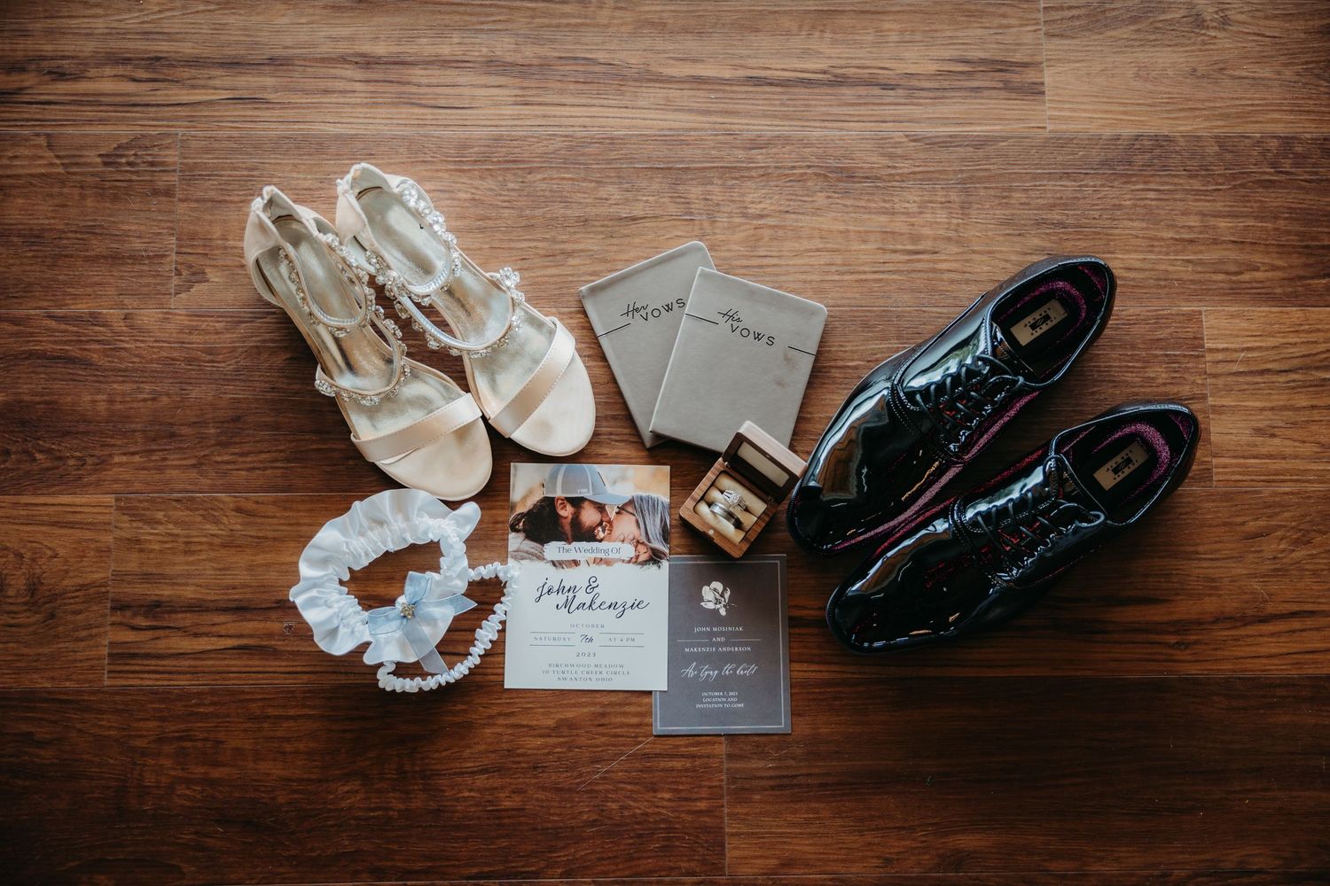 Wedding accessories including shoes, rings, and invitations arranged on wooden floor.