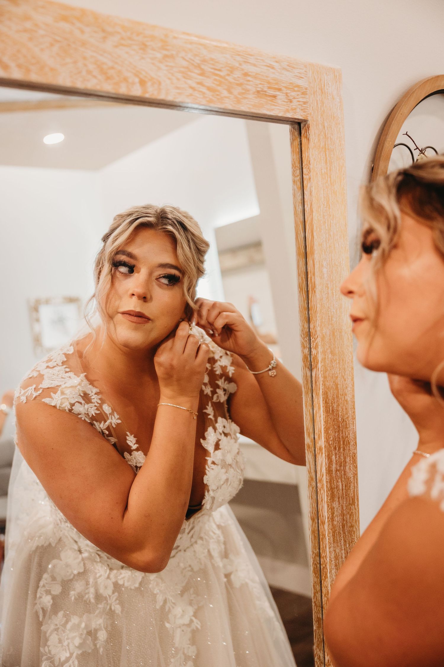 Reflection of bride putting on earrings in rustic mirror.