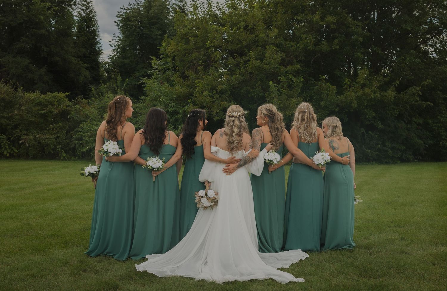 Wedding party in mint green dresses and white gown posing together on grassy lawn.