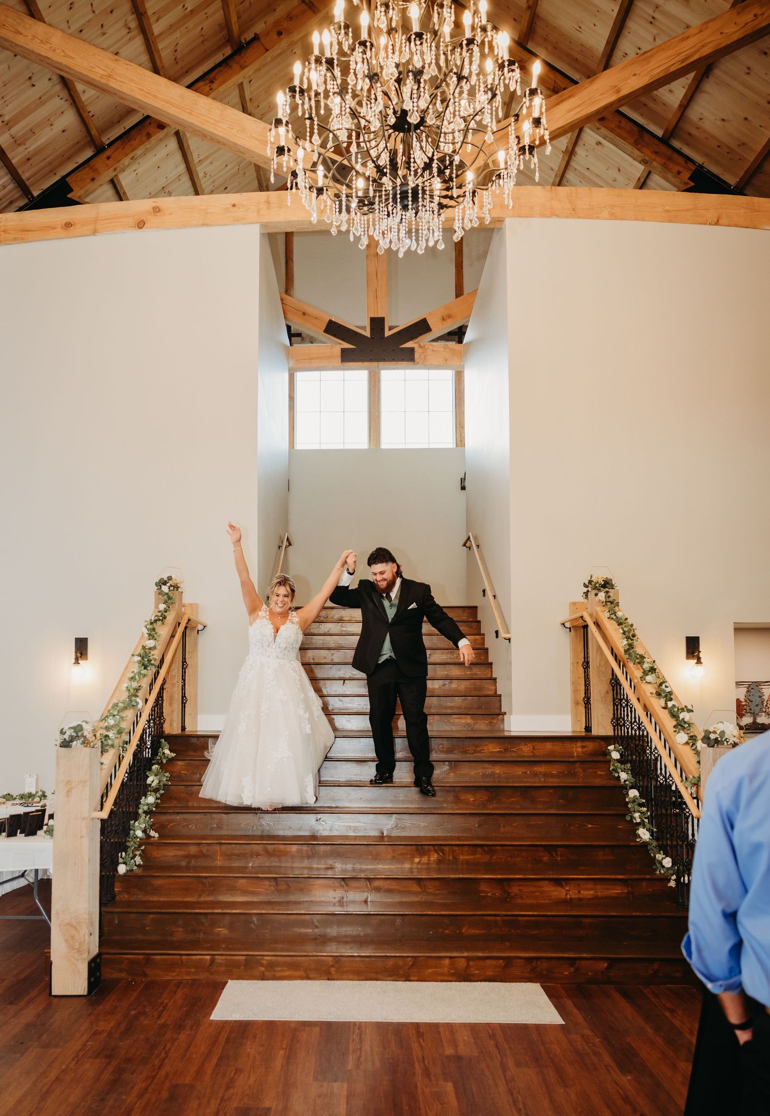 Grand staircase decorated with garland under crystal chandelier at wedding venue.