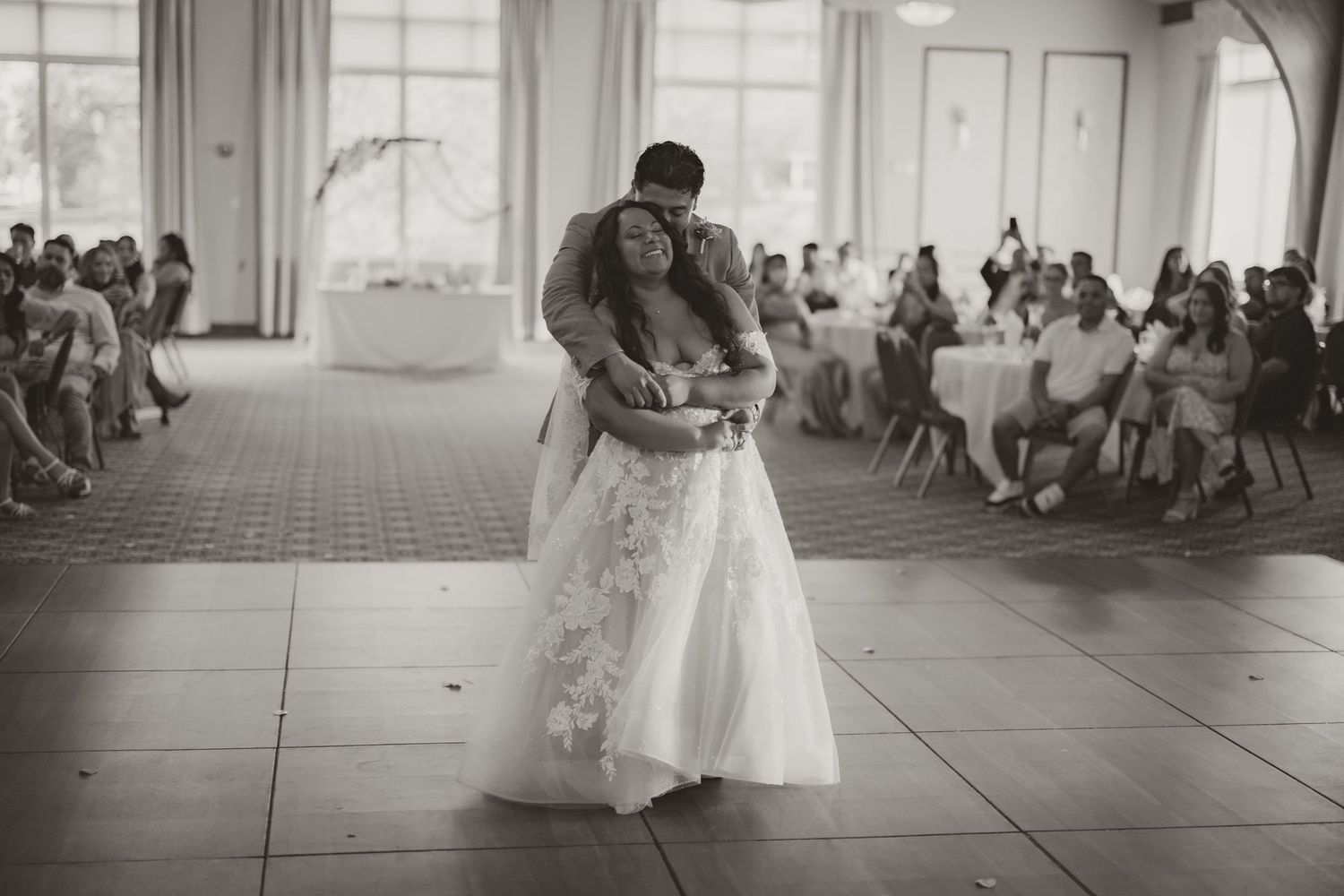 A couple shares their first dance at their wedding reception in an elegant ballroom filled with guests.