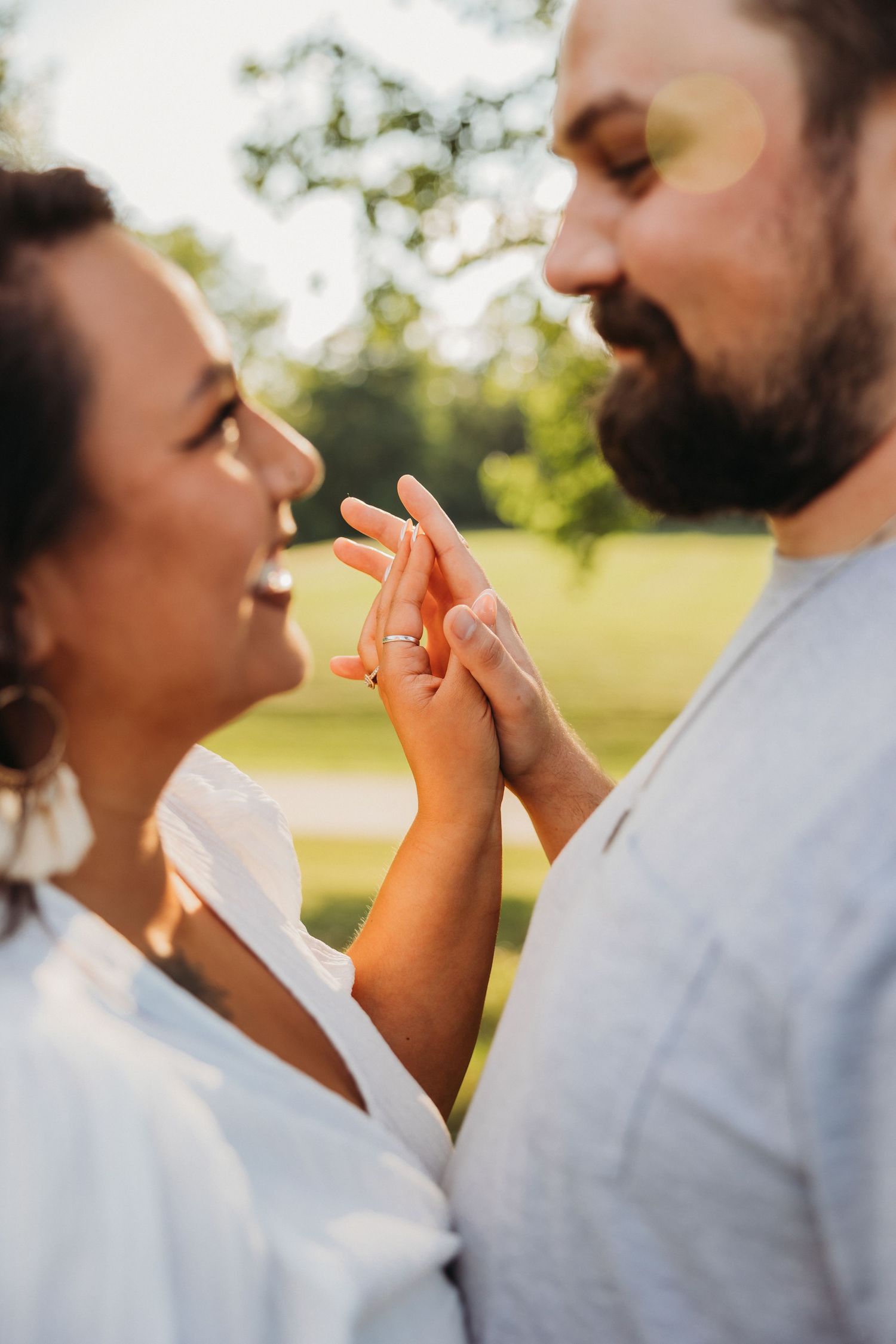 Joyful couple sharing an intimate moment outdoors in white attire with sunlit background.