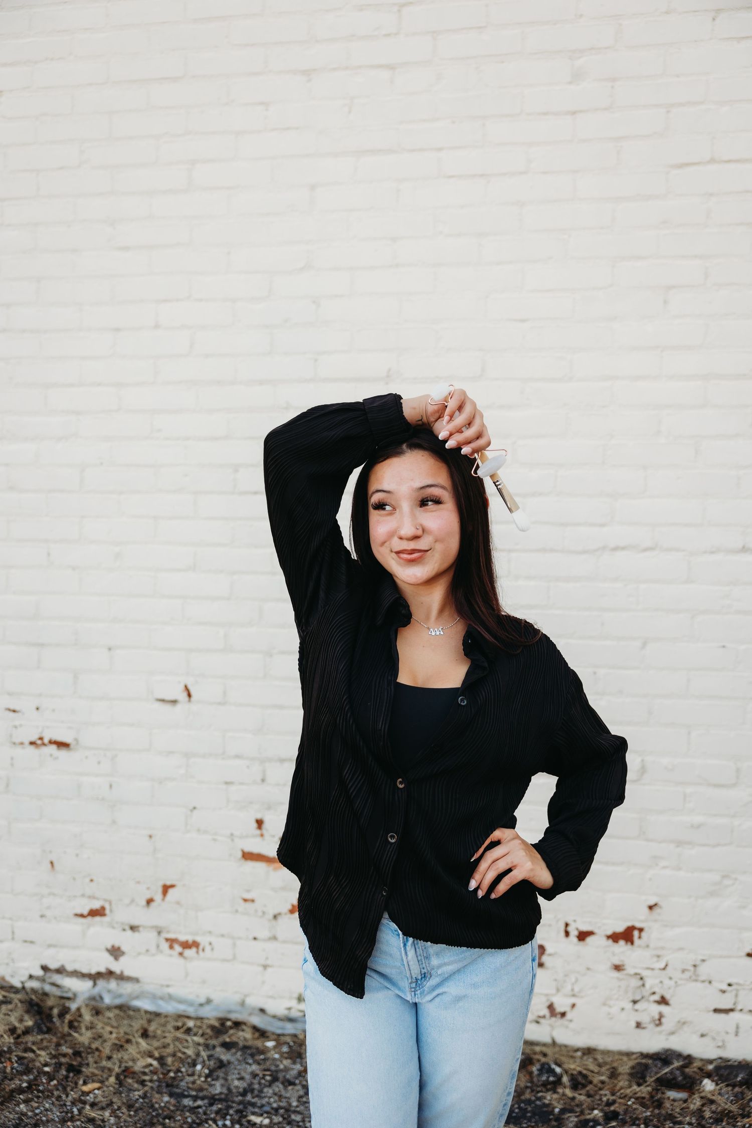 Casual portrait of woman in black cardigan and jeans posing against white brick wall background.