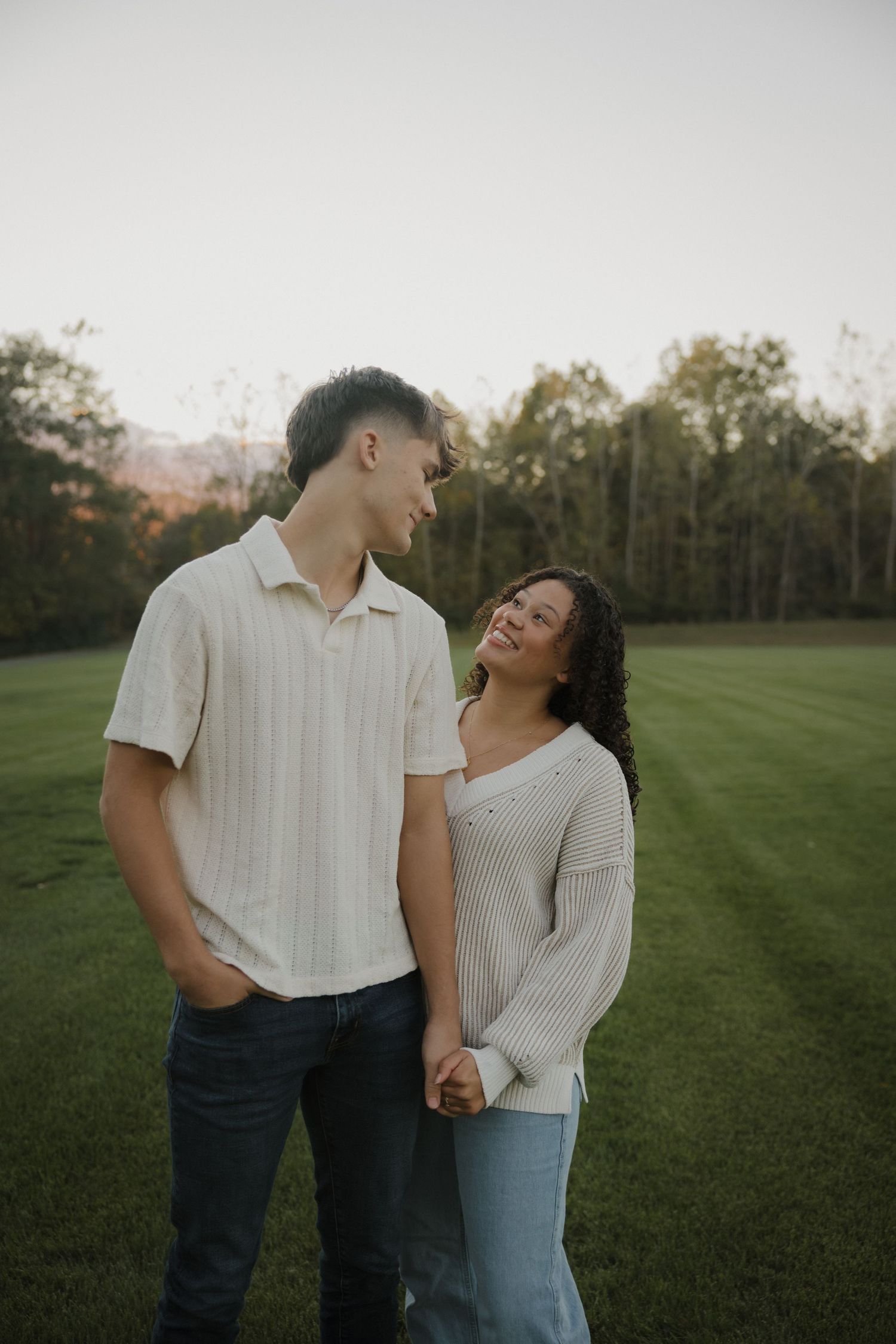 A couple shares a tender moment together in a grassy field during golden hour.