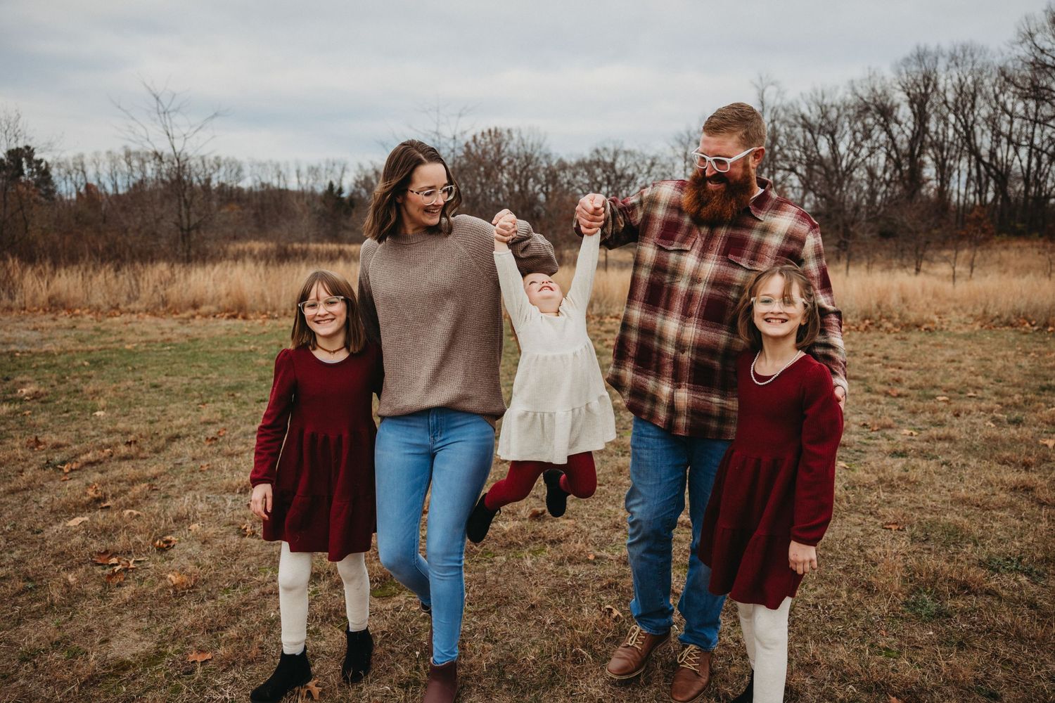 Joyful outdoor family portrait with parents and children in coordinating outfits standing in a rustic field.