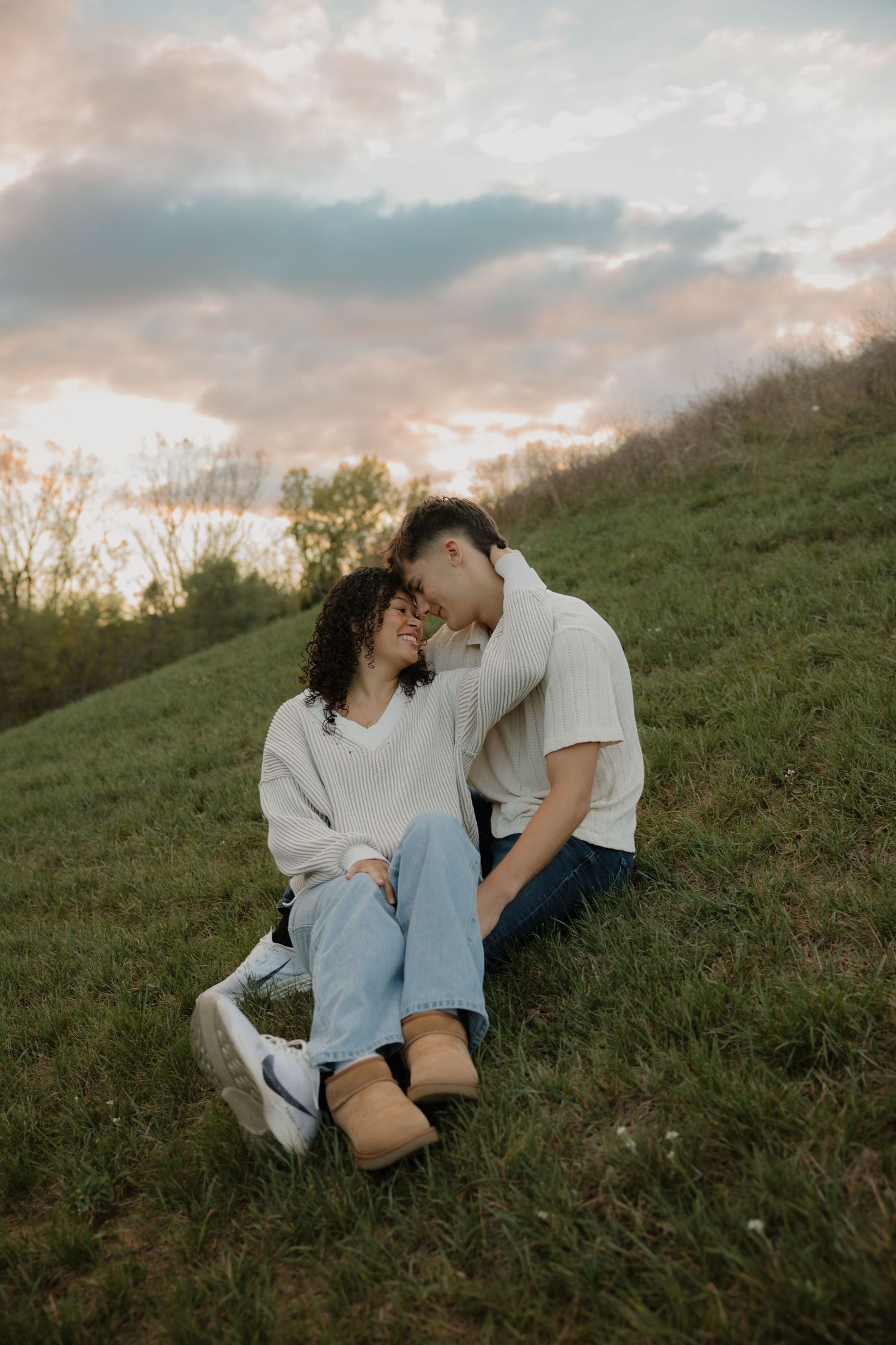 A romantic couple sitting together on a grassy hillside during golden hour.