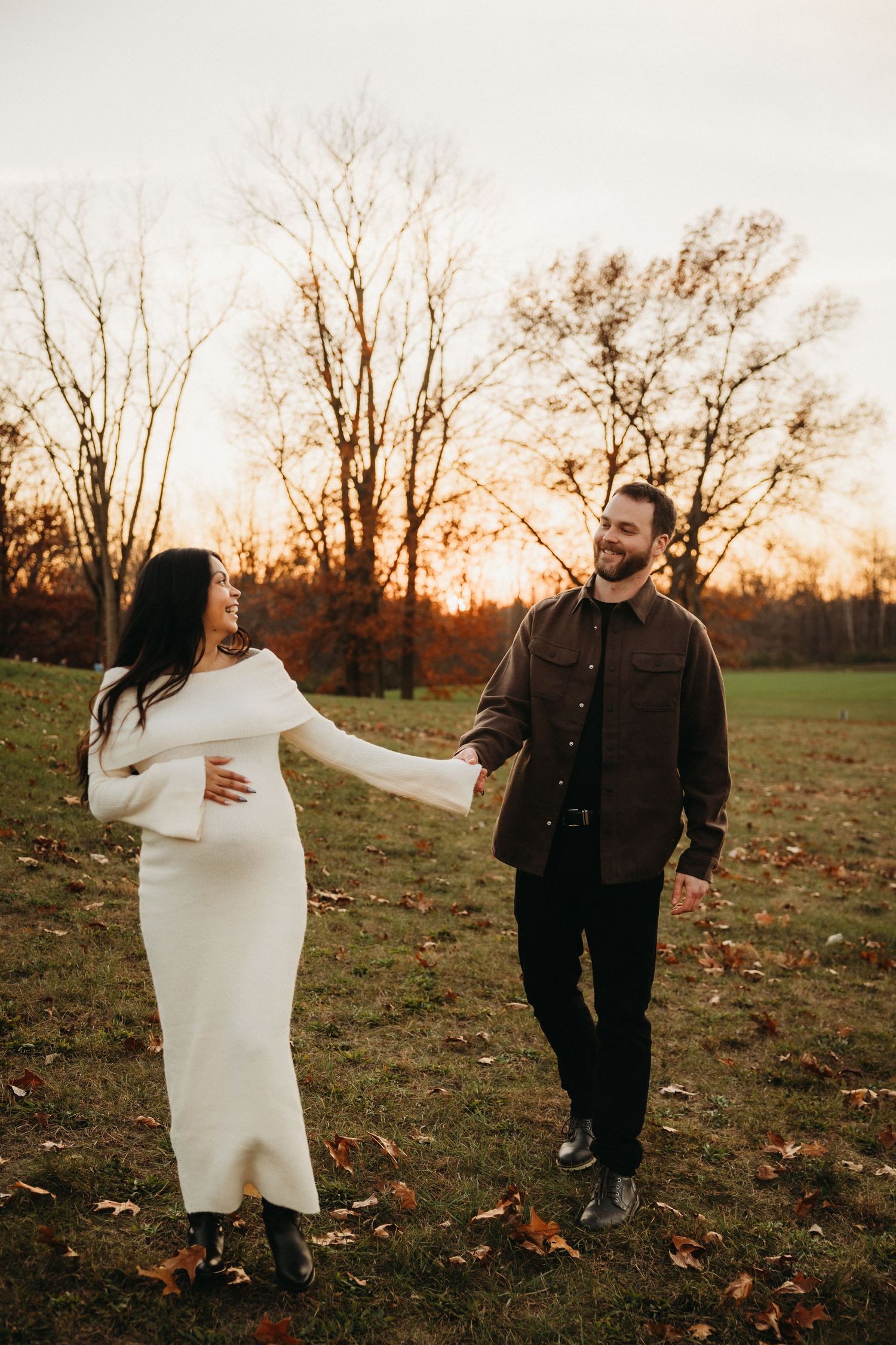 Couple in casual attire playing and laughing in autumn field at sunset.