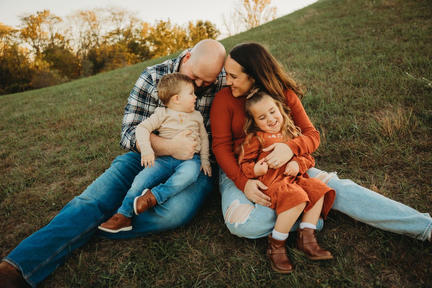 Intimate family moment captured on grassy hillside during sunset photo session.
