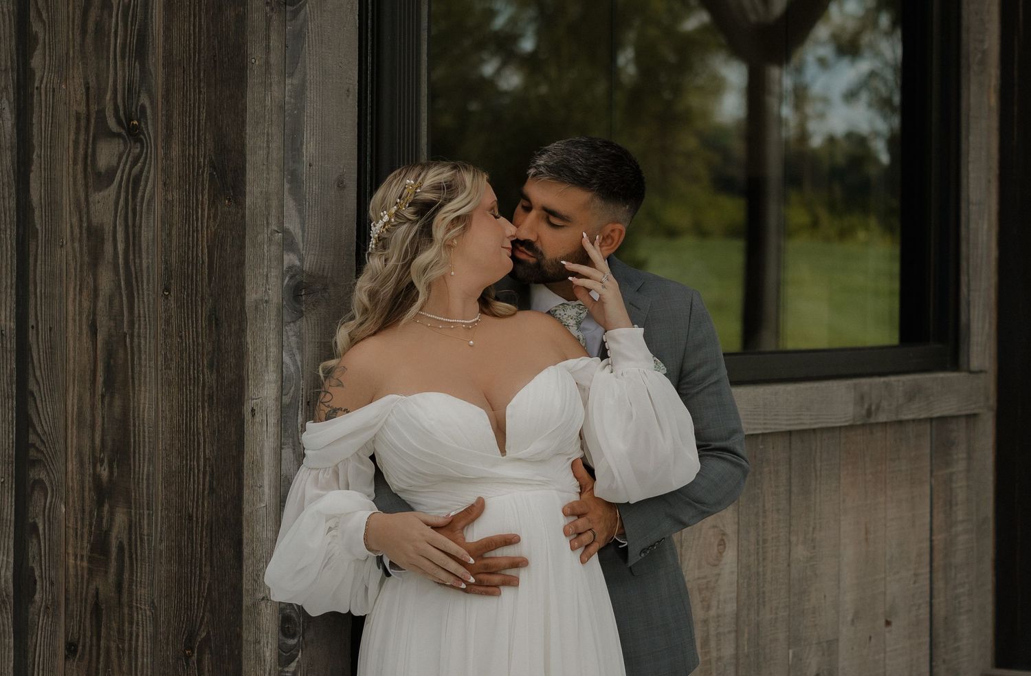 A romantic wedding couple embraces in front of a rustic wooden barn wall on their special day.