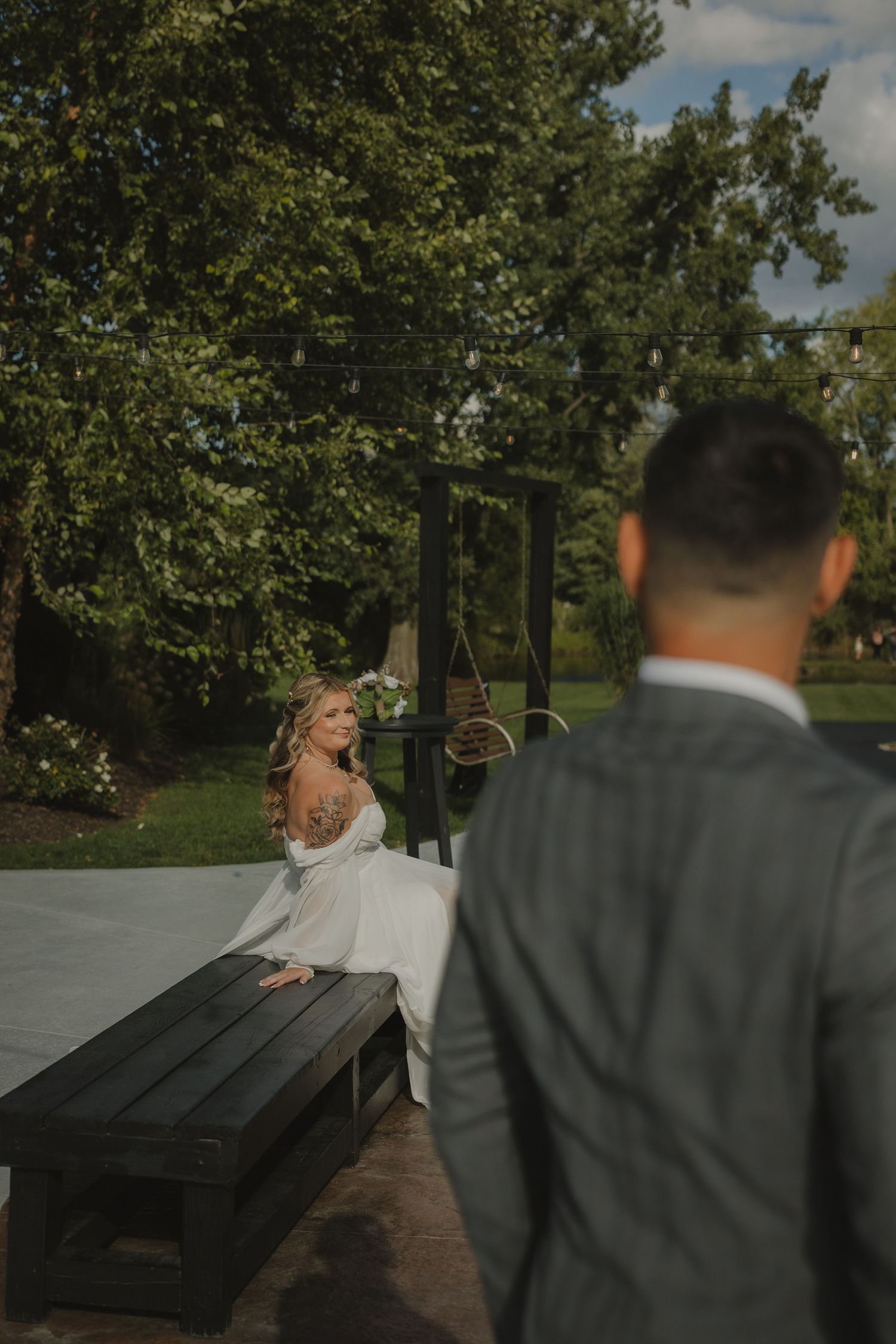 A couple shares a candid moment on a wooden bench in an outdoor garden setting.