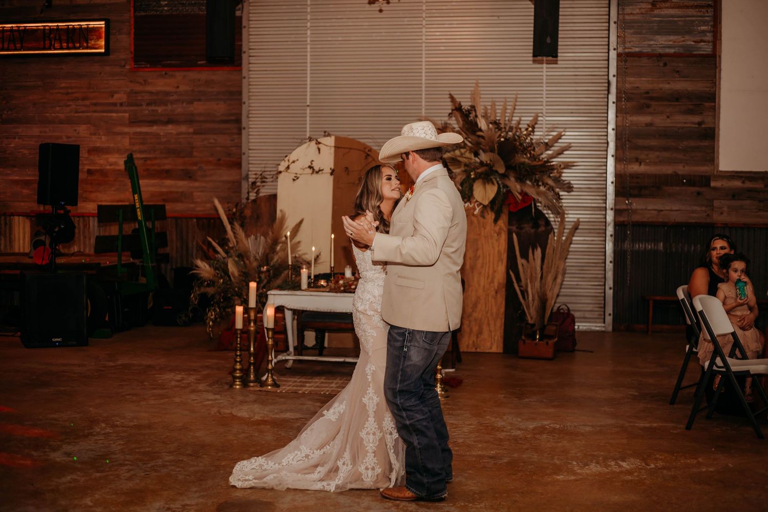 A newlywed couple shares their first dance in a rustic venue decorated with dried flowers and wooden accents.
