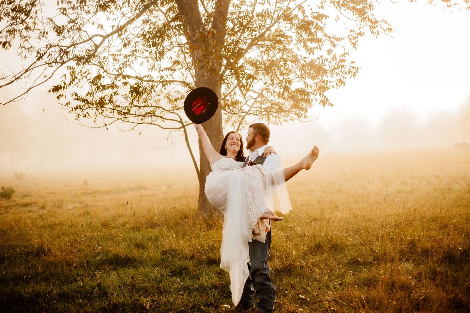 A romantic couple dances in a golden sunlit field beneath an autumn tree.