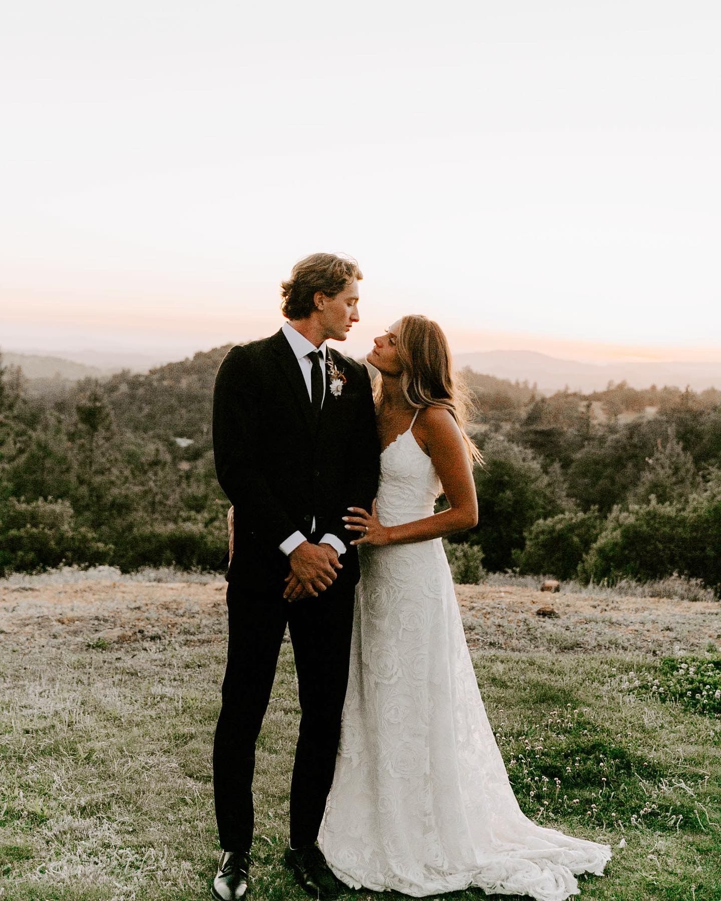 Newlyweds share intimate moment on hilltop during golden hour.
