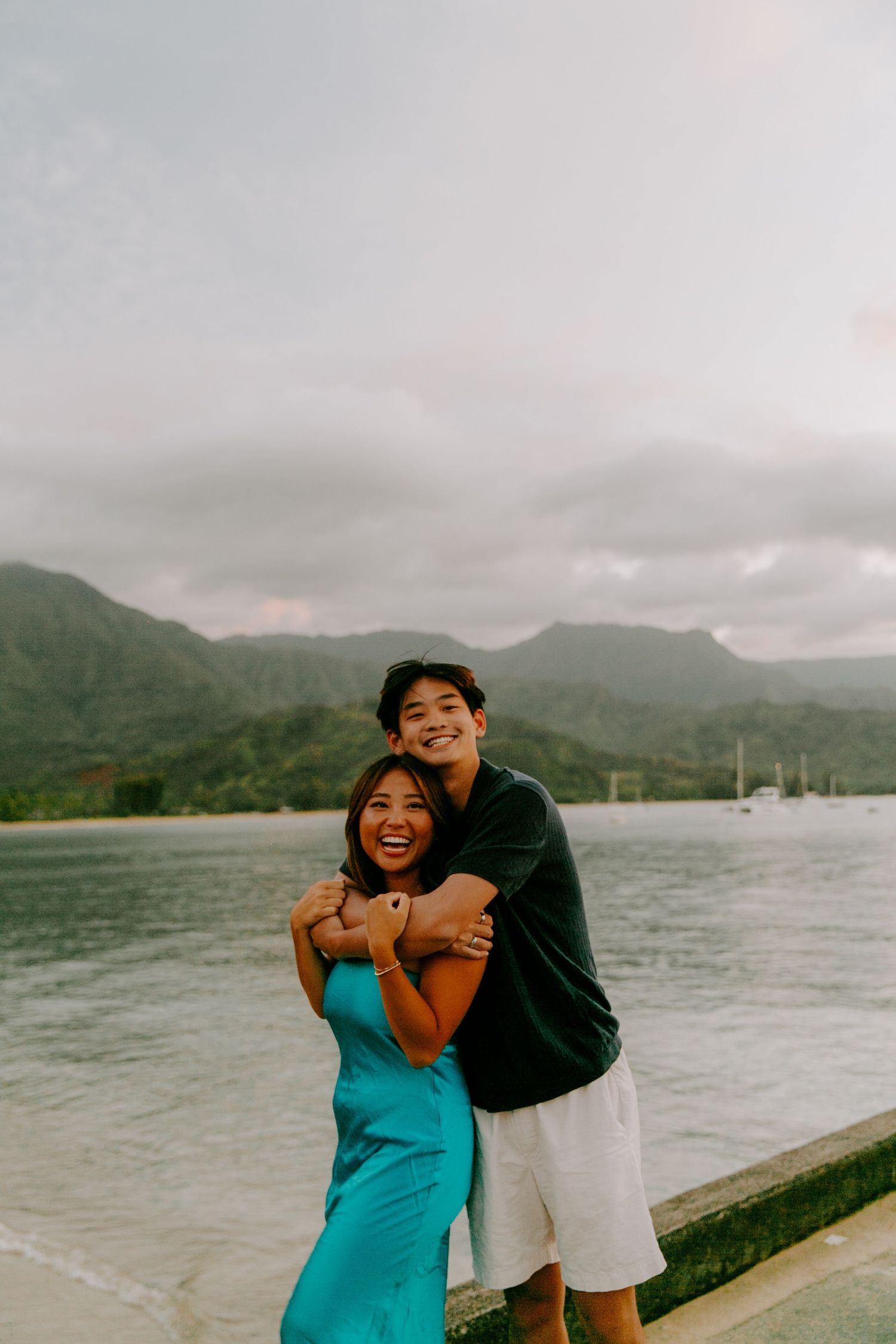 Couple laughing together by waterfront with mountains in background.