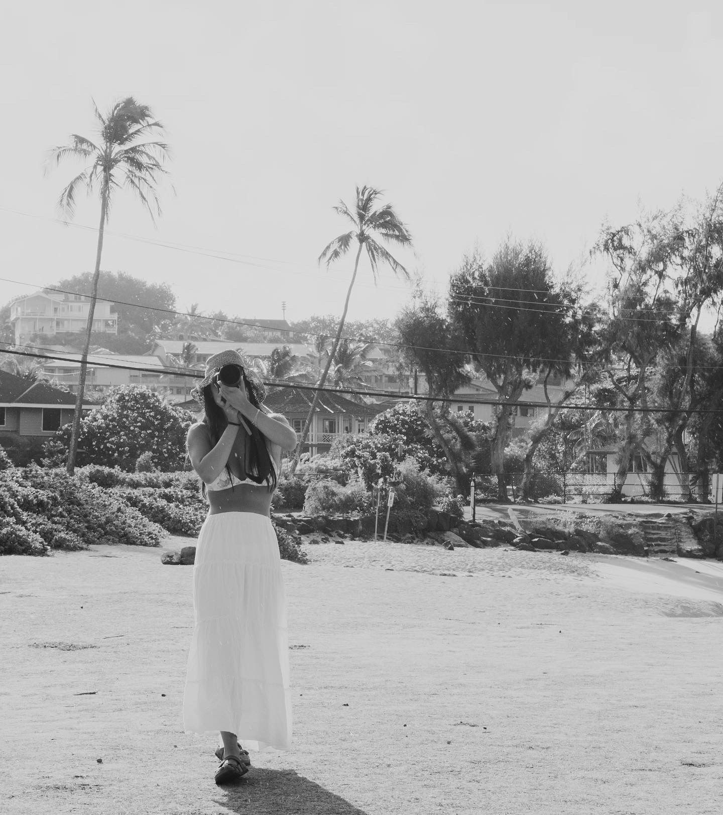 Black and white photo of a person standing among palm trees in a tropical landscape.