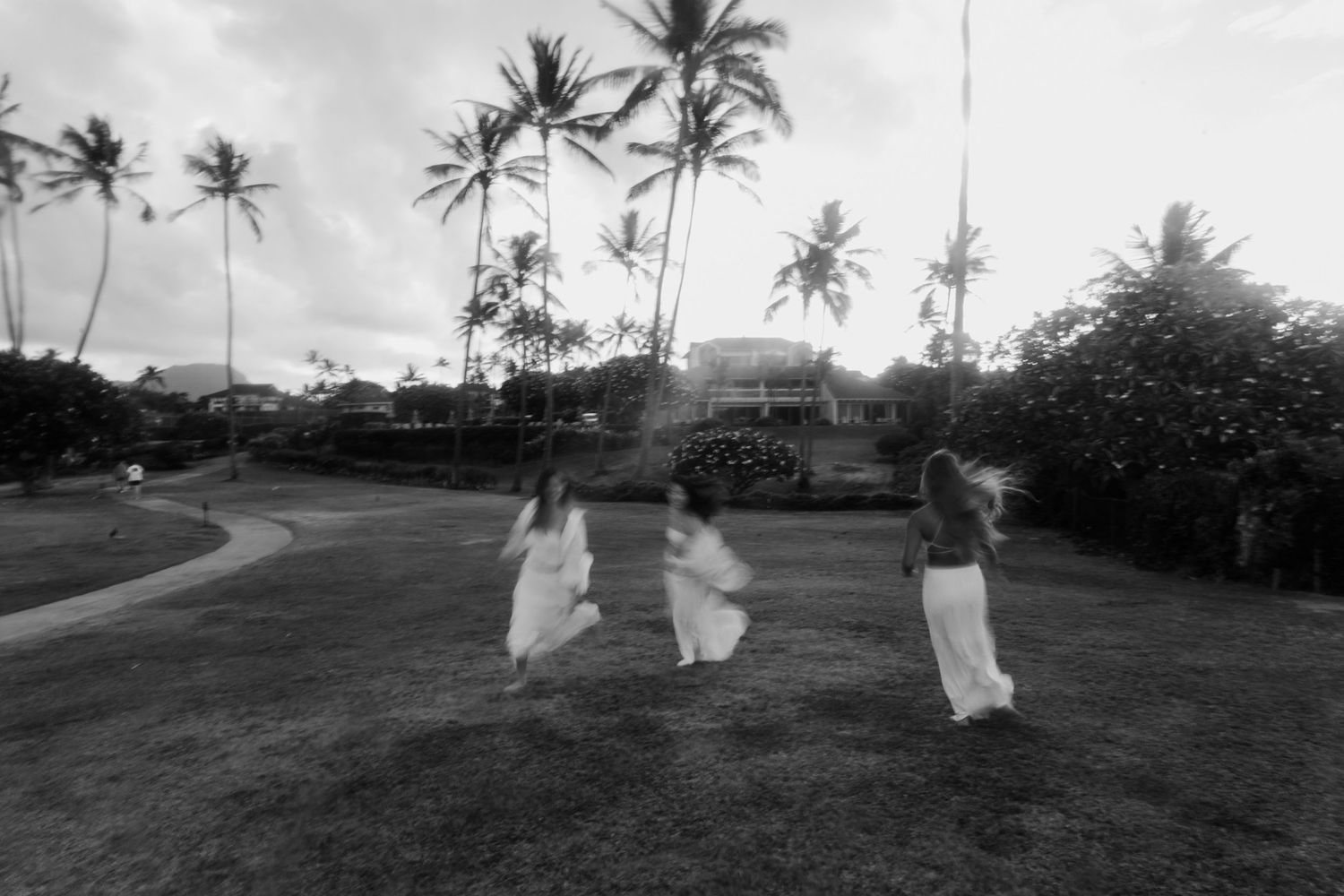 Black and white photo of three people jumping on grass field with palm trees.
