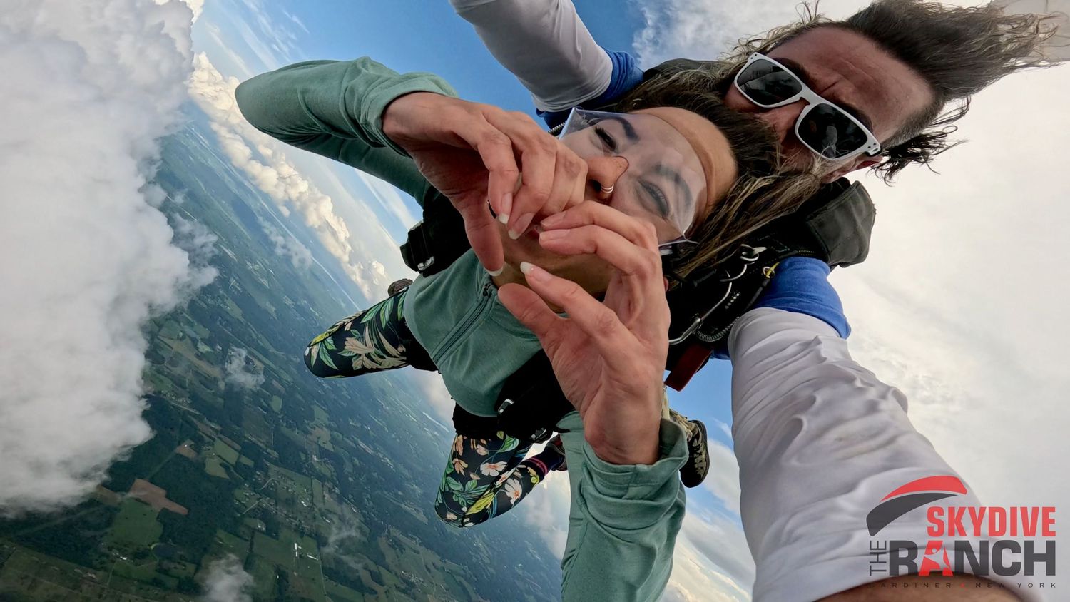A tandem skydiving pair falling through clouds above mountainous terrain during a thrilling jump.