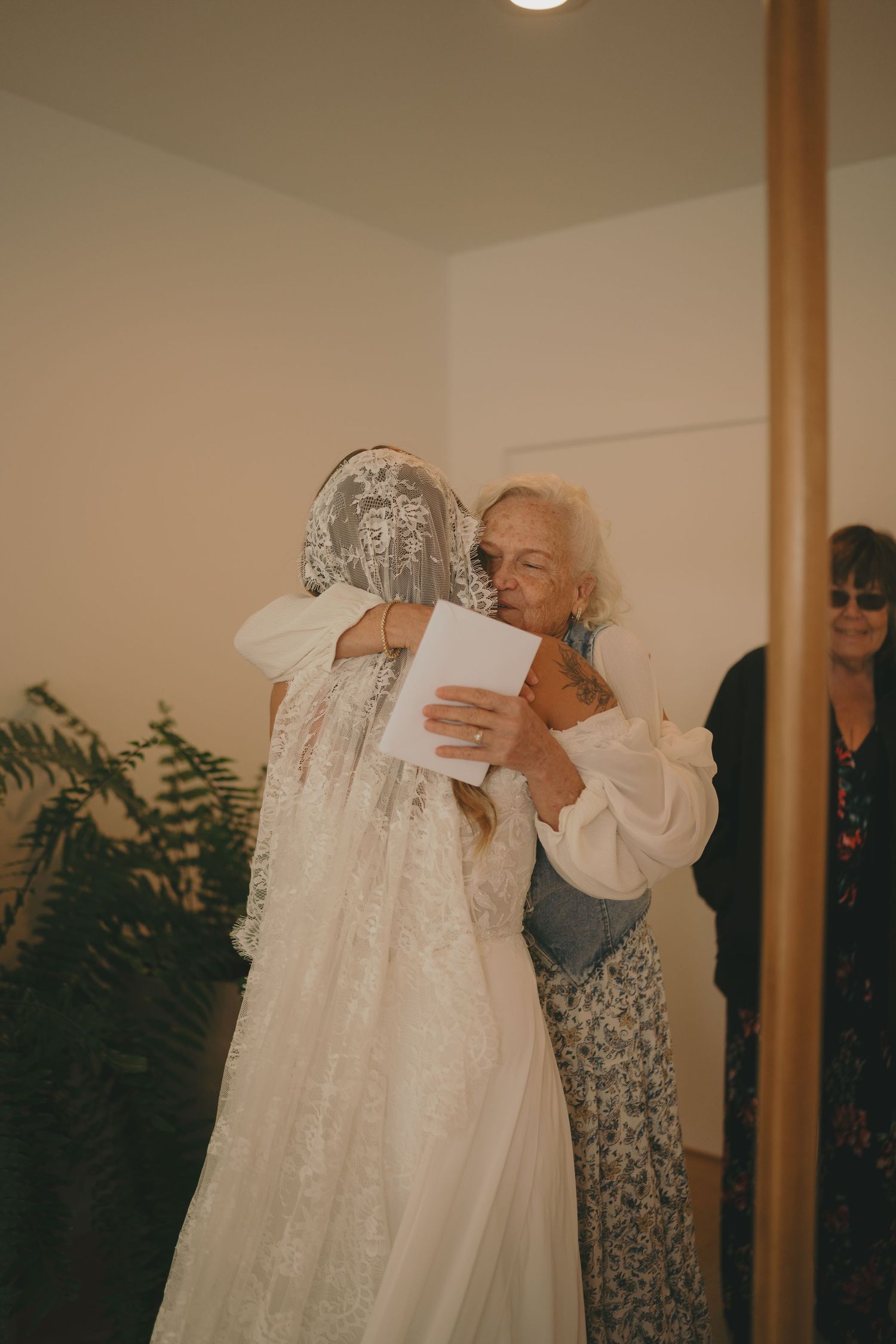 White lace wedding dress being held up and admired in an indoor setting.