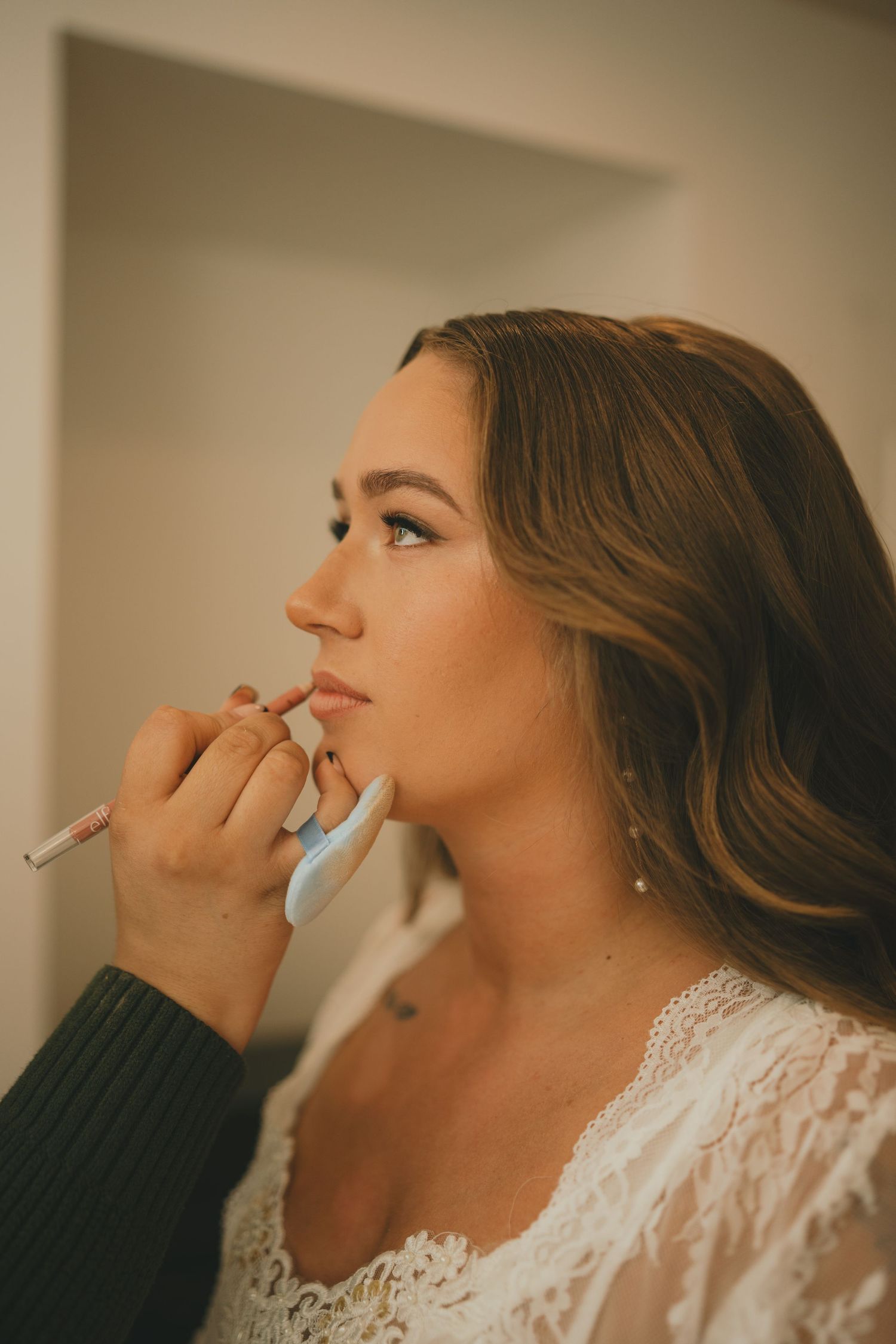 A makeup artist applies cosmetics to someone wearing a white lace top in a series of profile shots.