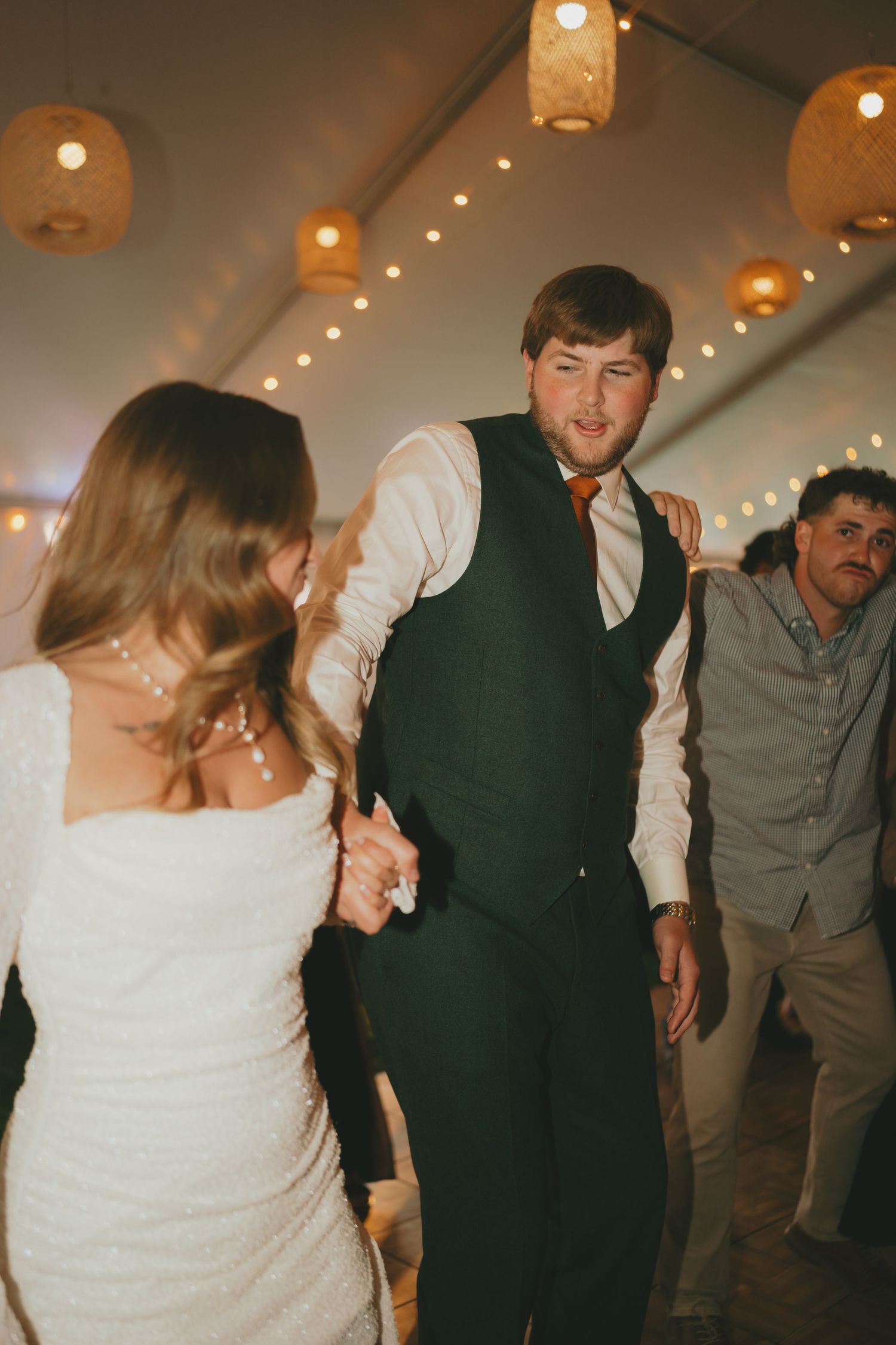 Wedding guests dance together on a dimly lit dance floor with glowing paper lanterns overhead.