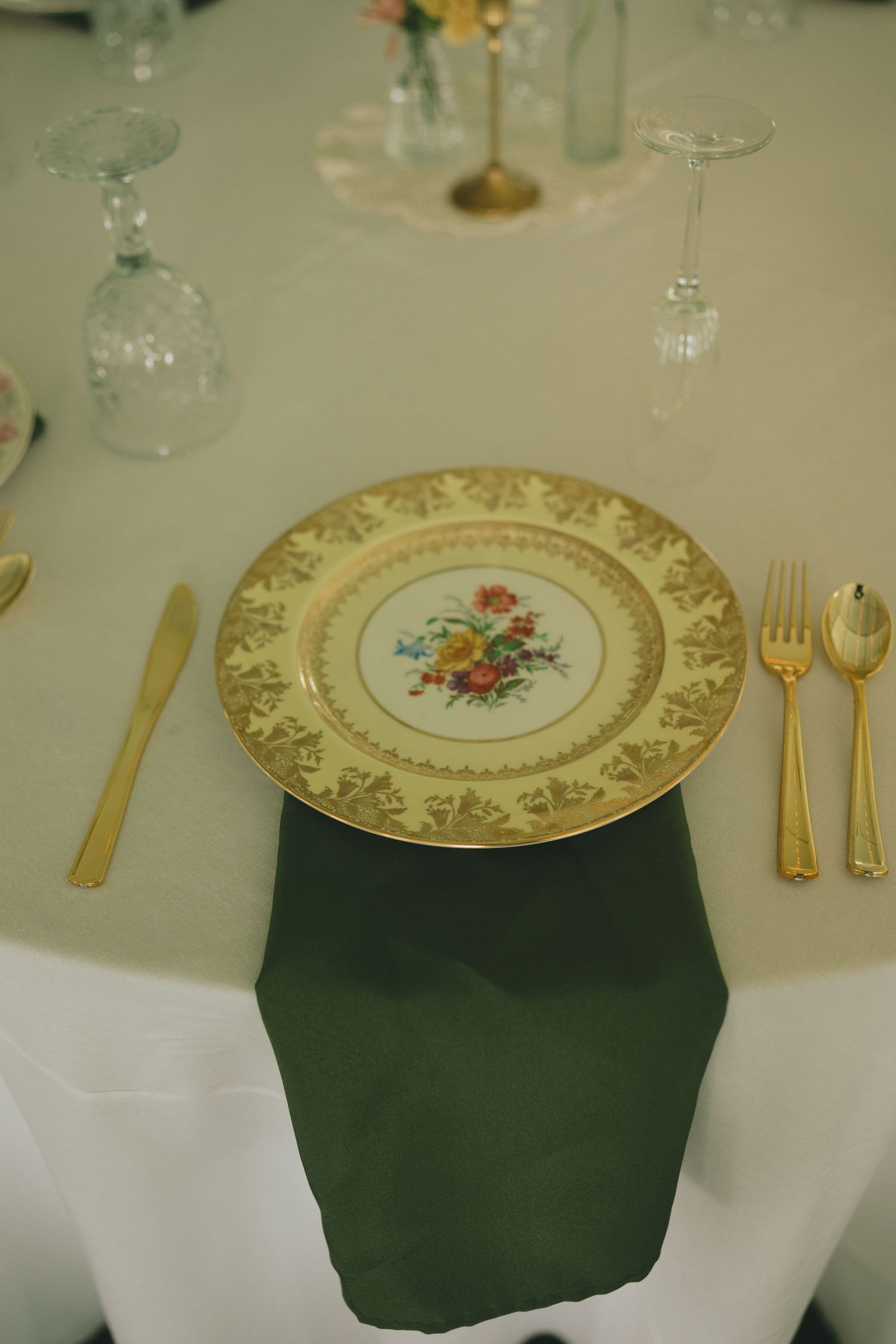 Elegant place setting with ornate gold-rimmed plate featuring floral design and gold utensils on green napkin.
