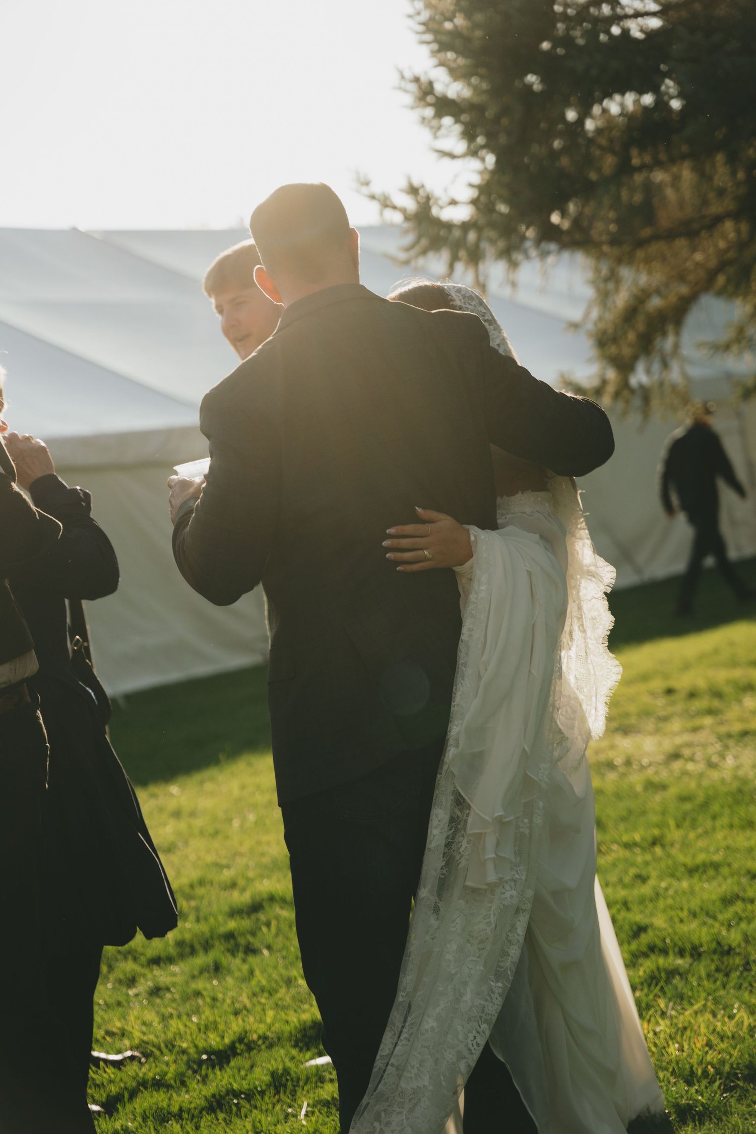A romantic silhouette of a couple embracing on a grassy hillside during golden hour with sunlight glowing behind them.