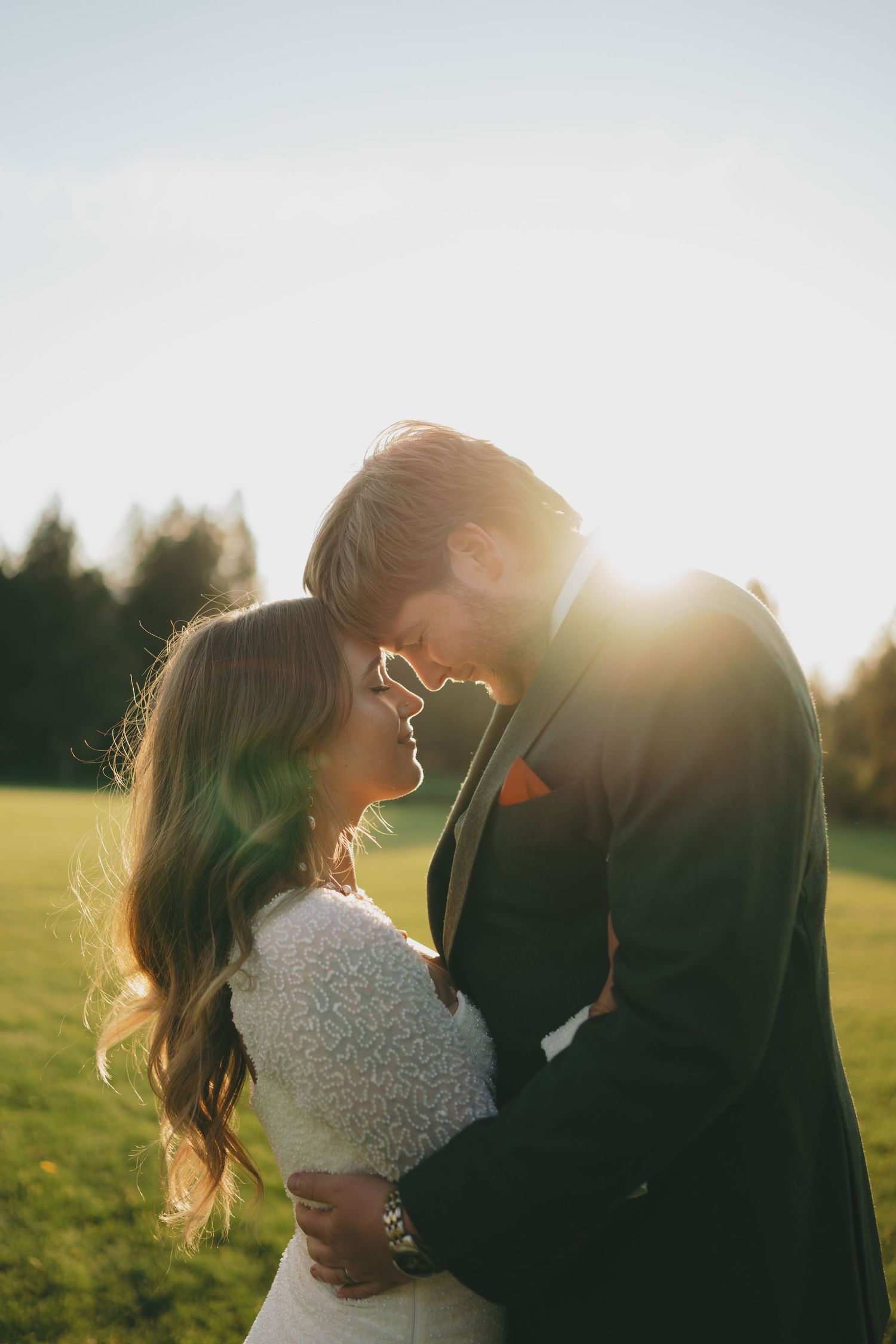 Romantic couple embraces in a sunlit field during golden hour, creating a dreamy silhouette against the warm sky.