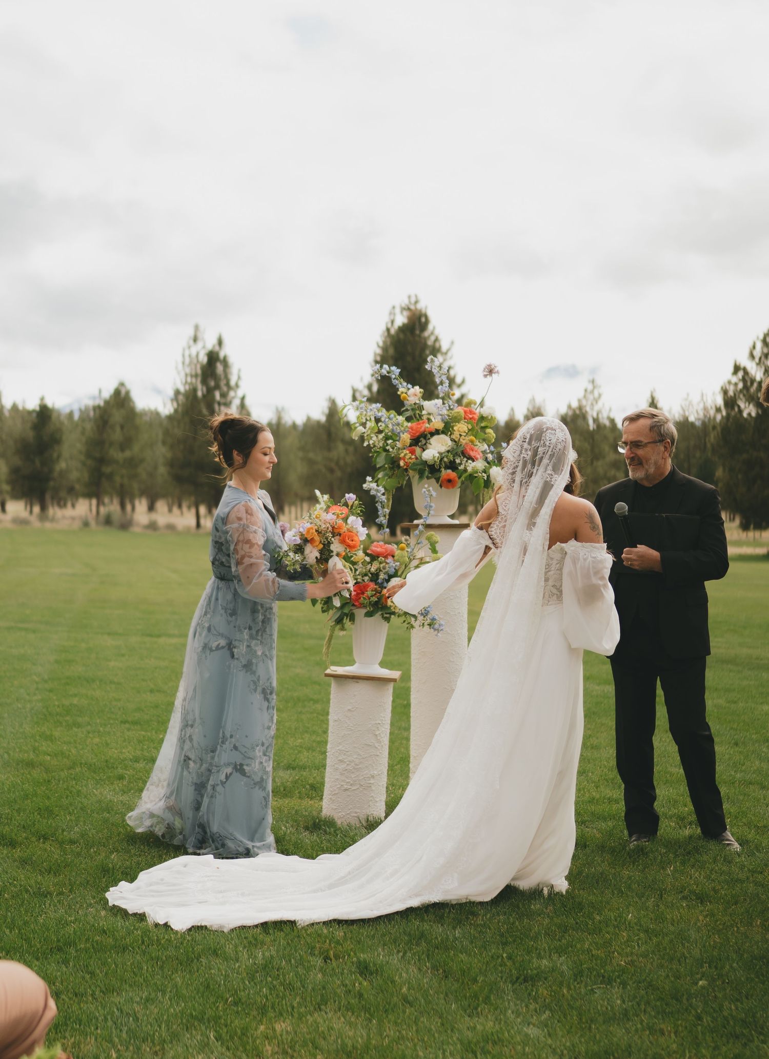 Romantic outdoor wedding photoshoot in a green field with floral arrangements and elegant decor elements.