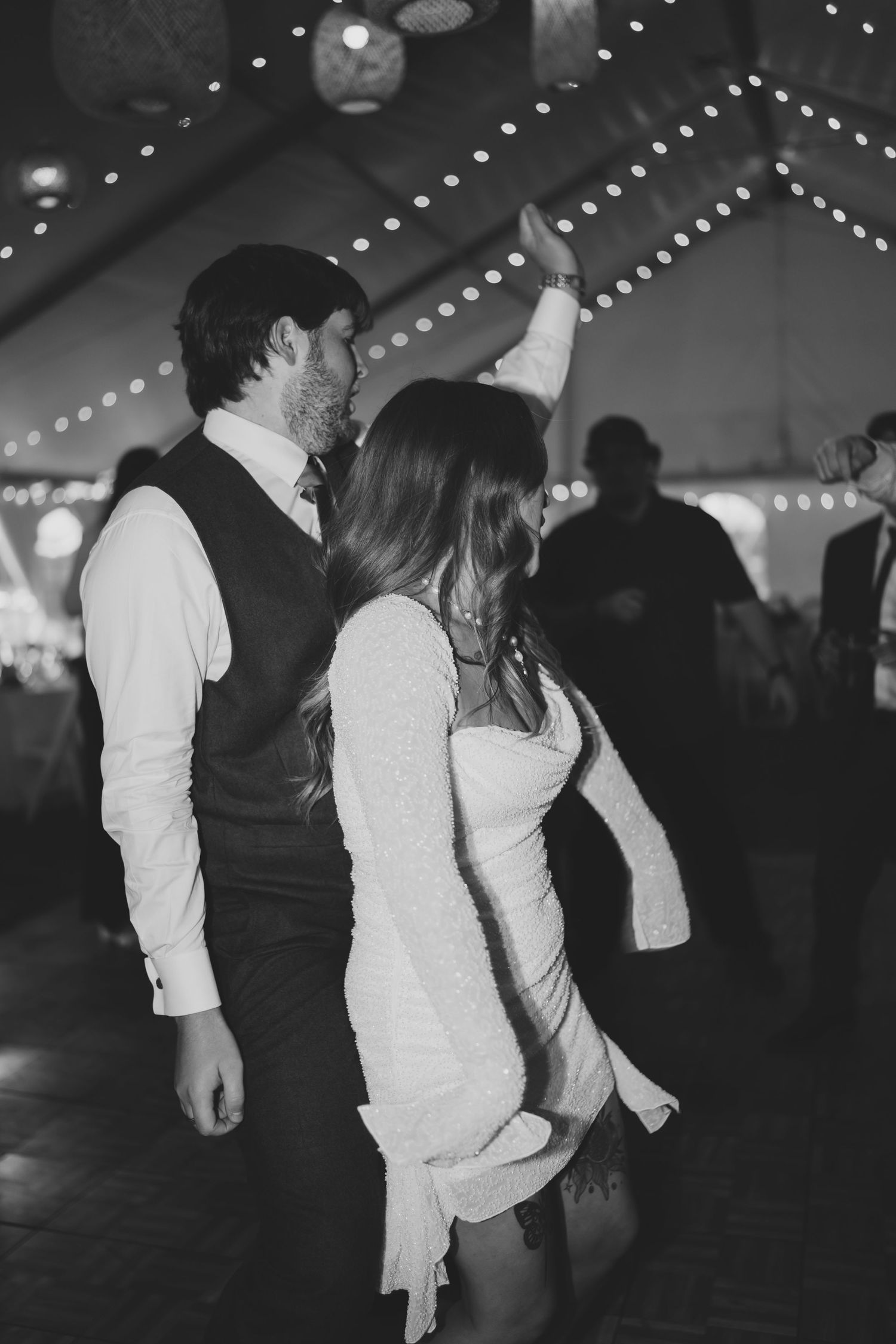 Black and white photo of dancing at a wedding reception under twinkling lights.